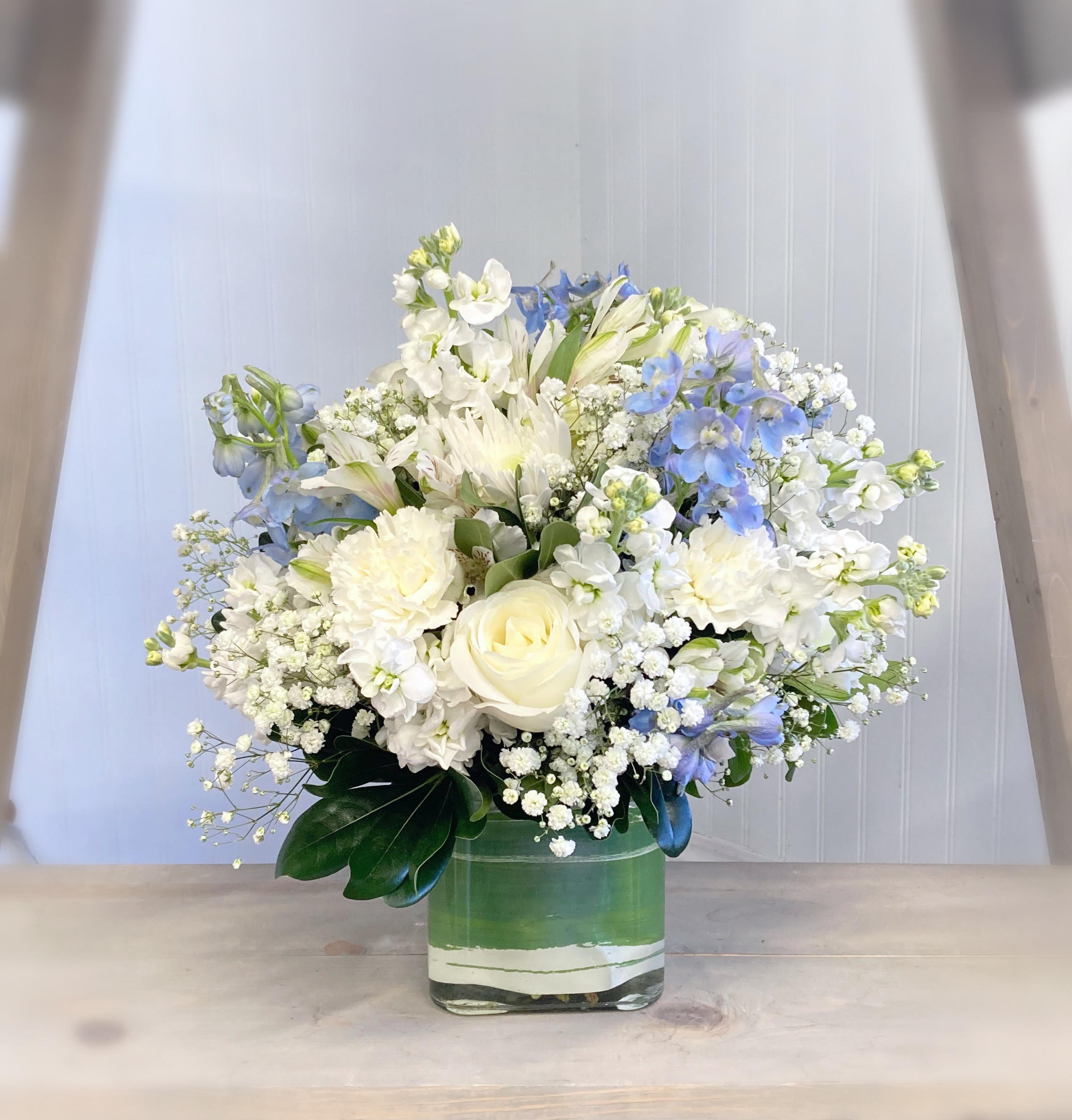 White and blue mixed flower arrangement in a square glass vase
