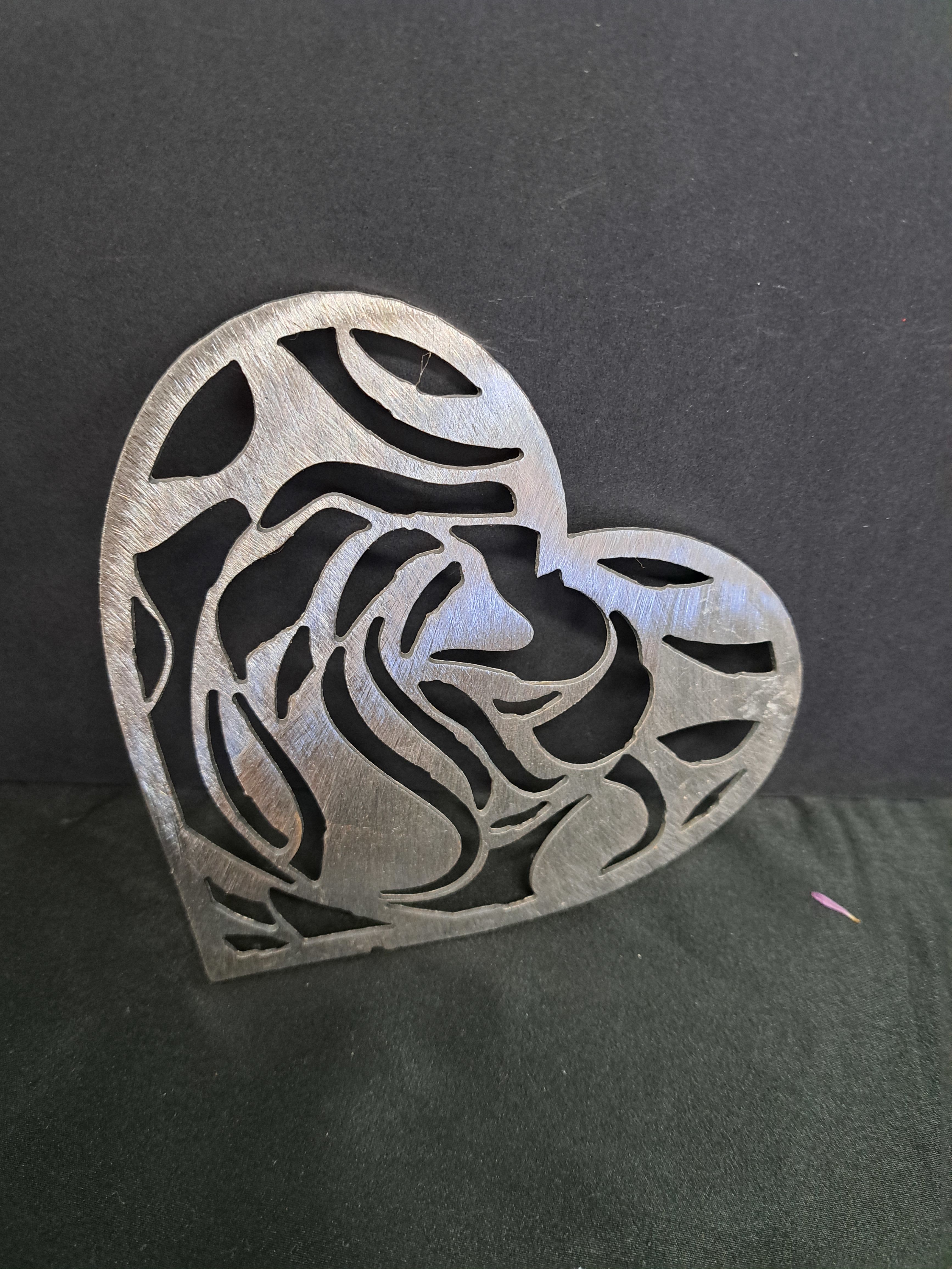 Metal Heart wall hanger Full rose - A modern metal heart wall hanger that doubles as a heartfelt gift for Valentine's Day or an anniversary, this compact heart-shaped decor piece brings contemporary romance to any shelf or mantel. The openwork floral pattern cut through the brushed silver surface catches light and shadow, creating a subtle, textured focal point that feels both elegant and slightly rustic - the kind of accent that makes the person you're thinking of smile every time they pass it. 