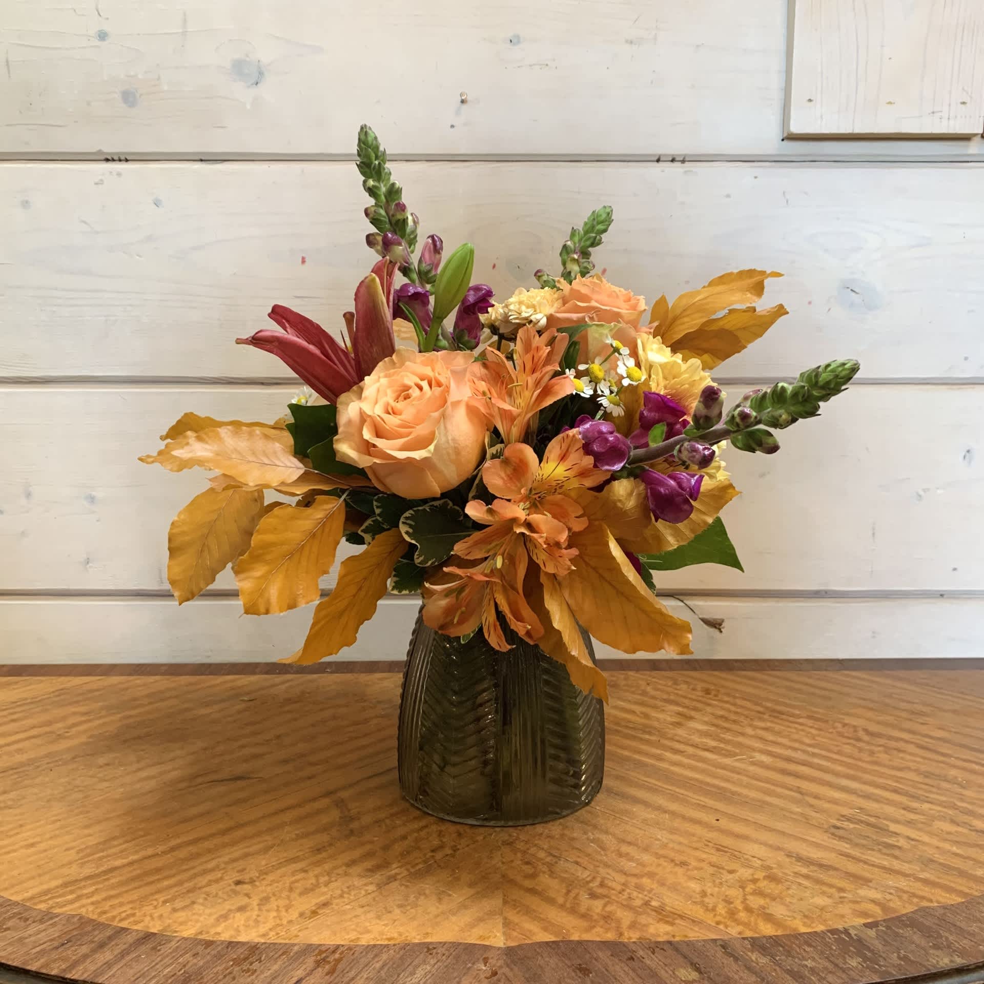 Autumn bouquet of peach and purple flowers in a dark glass vase