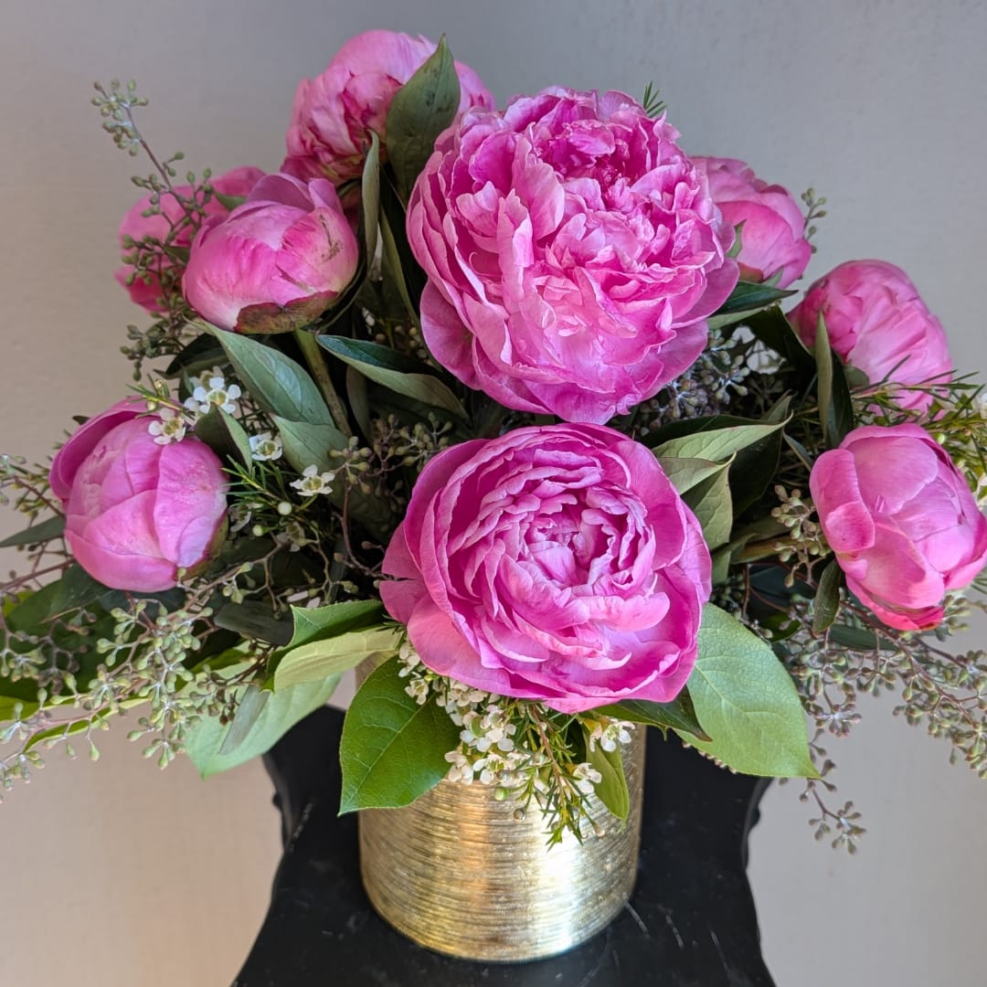 Pink peonies arranged in a gold vase with small white filler flowers