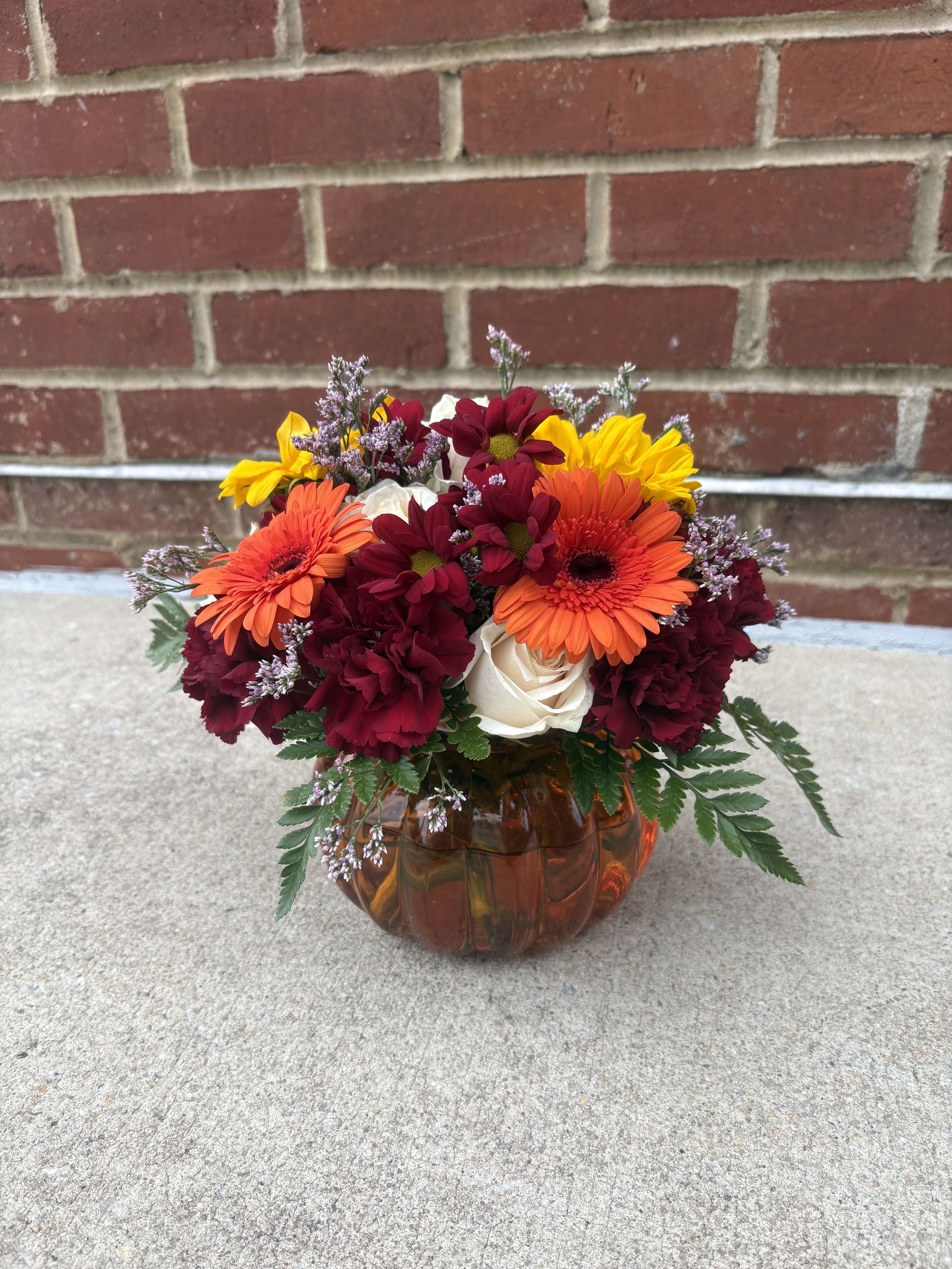 Mixed bouquet in an amber glass pumpkin vase with orange, yellow, burgundy, and white blooms
