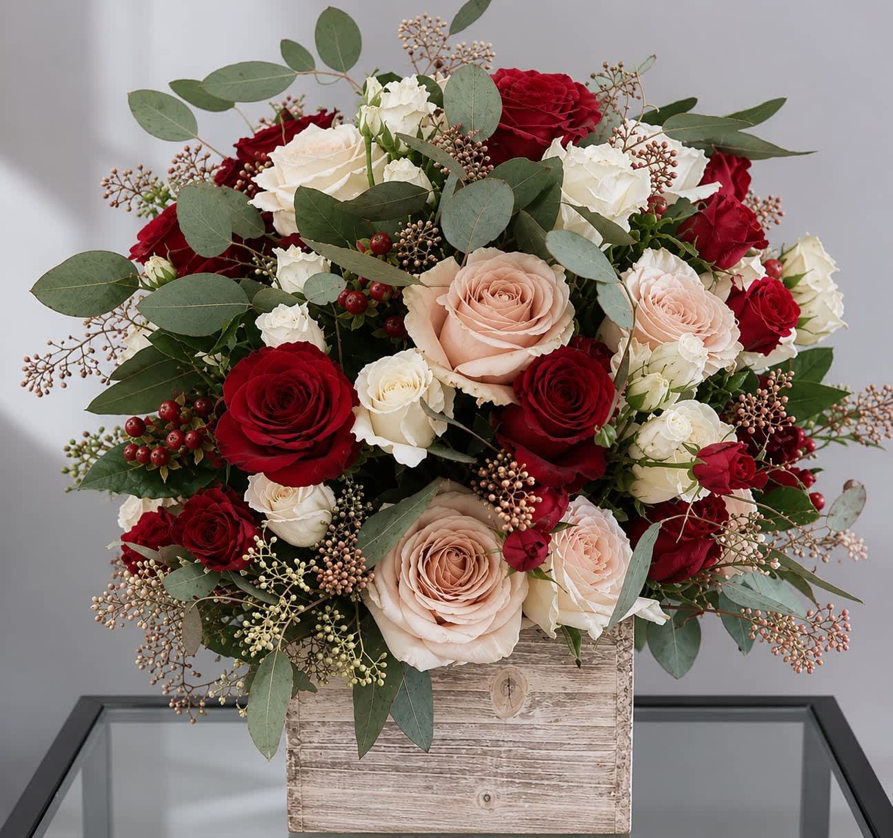 Beautiful Romance - A timeless arrangement of premium roses in deep red, soft blush, and creamy white accented with eucalyptus, and delicate seed sprays. Presented in a rustic wooden box, this bouquet brings elegance and warmth to any space.