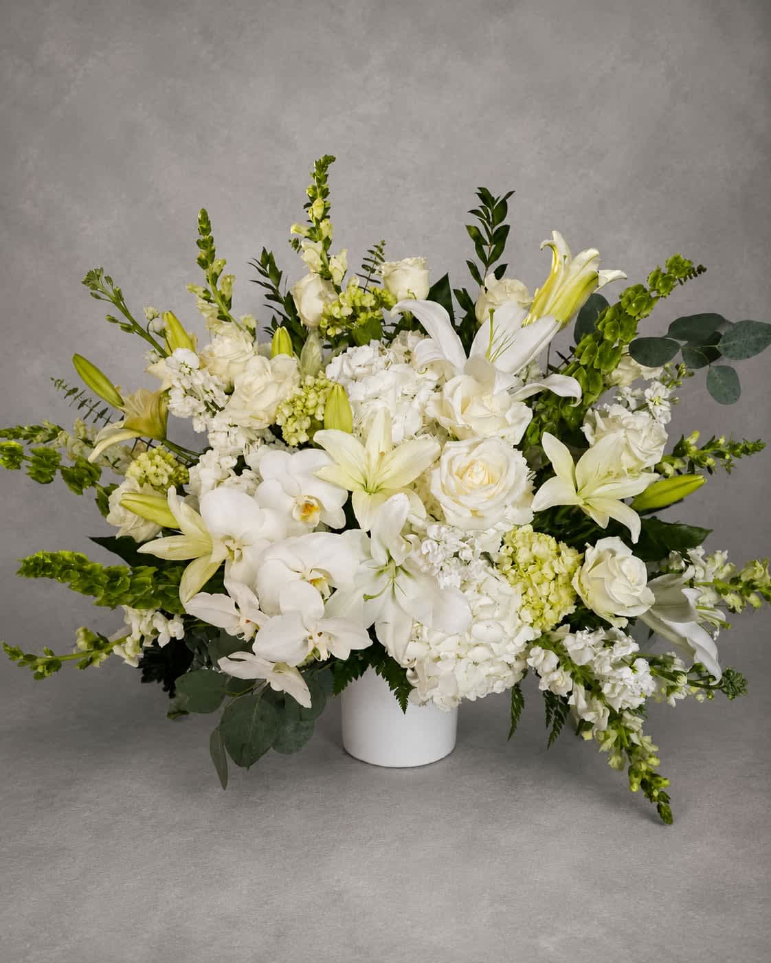Eternal Grace - An abundant arrangement of white orchids, lilies, roses, hydrangea, and premium blooms designed to convey beauty, comfort, and serenity. Eternal Grace offers a timeless tribute for life's most meaningful moments.