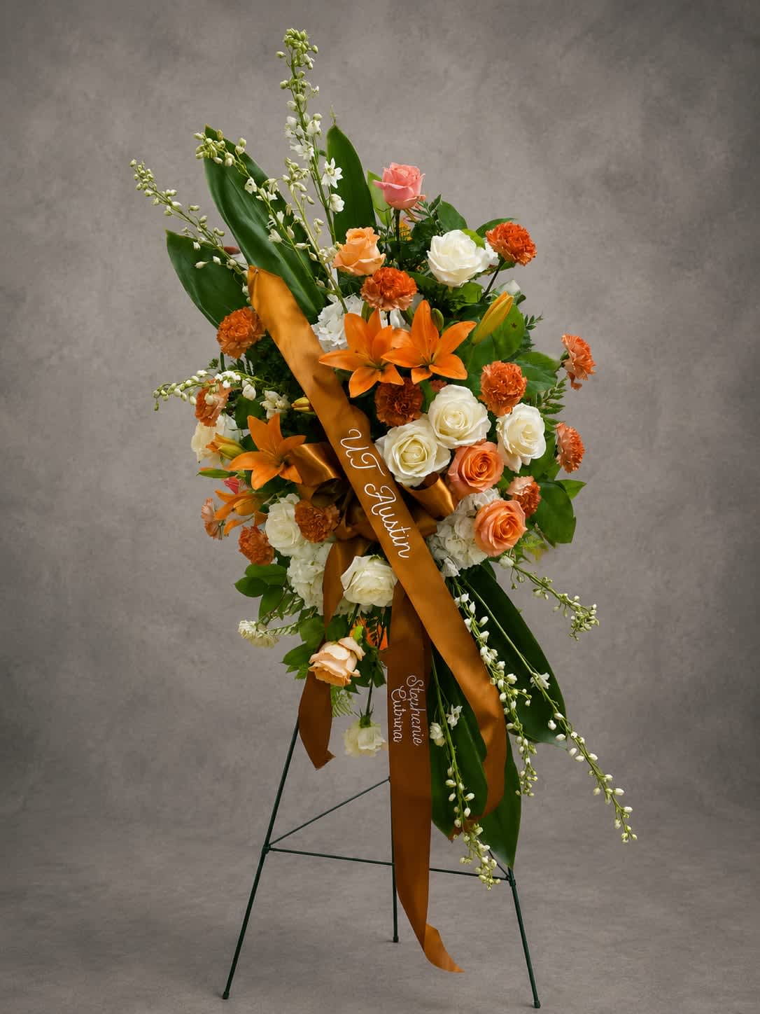 Longhorn Legacy - Inspired by a lifetime of friendships and cherished memories, Longhorn Legacy features vibrant orange lilies, peach and ivory roses, and seasonal blooms arranged in a graceful standing spray. A meaningful tribute honoring a life that touched many others.