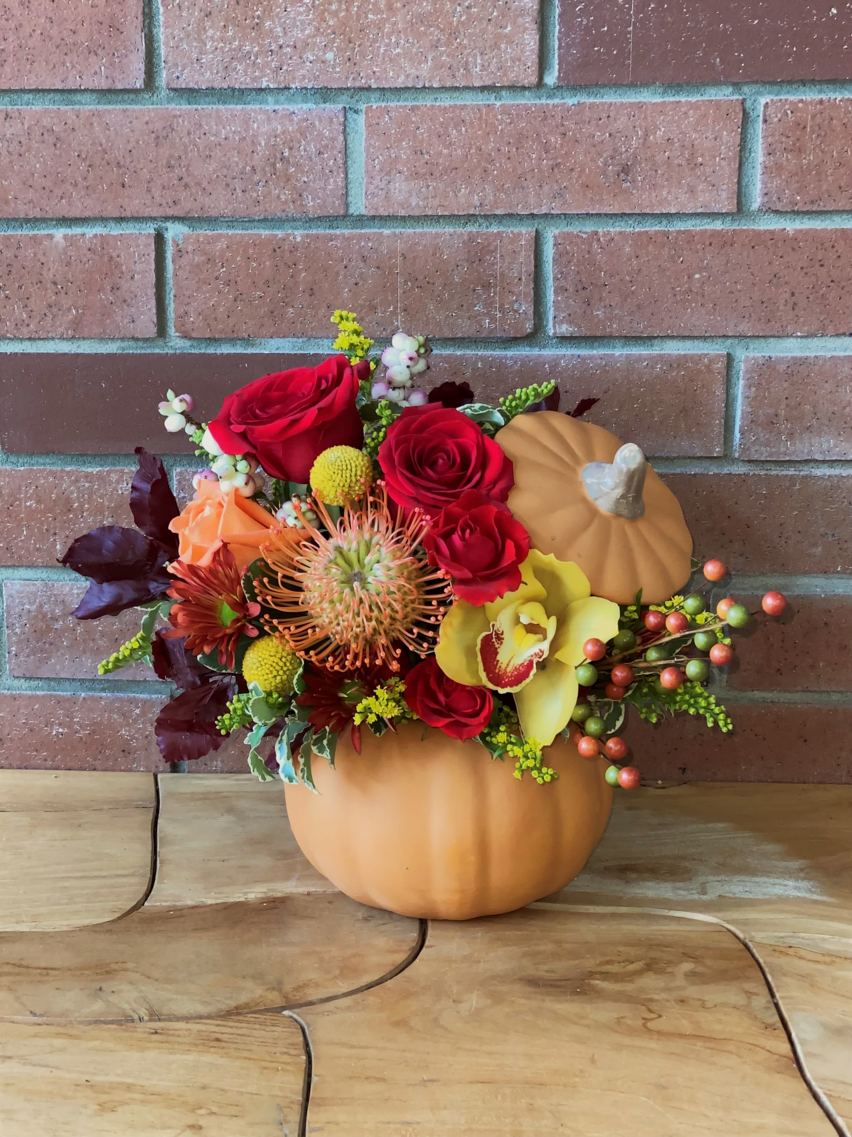 Fall floral arrangement in a pumpkin container with red roses and yellow orchid