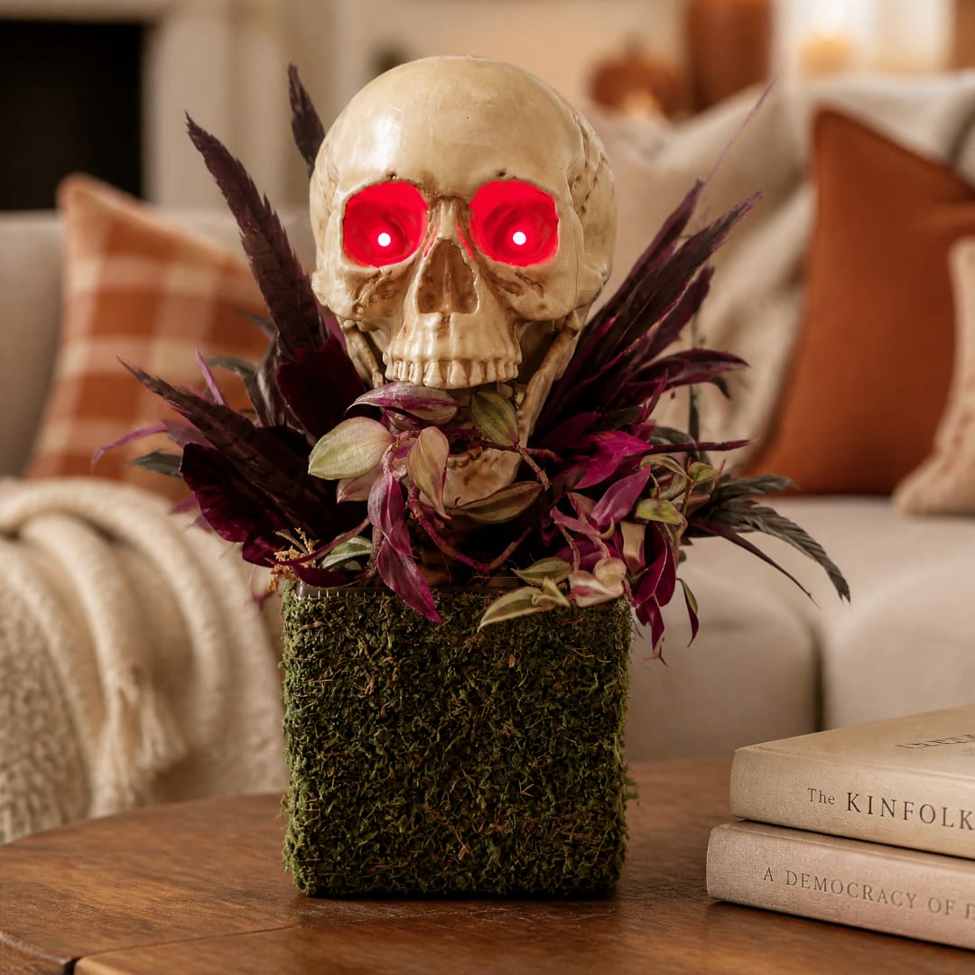 Skull decoration with glowing red eyes and purple foliage in a moss-covered container