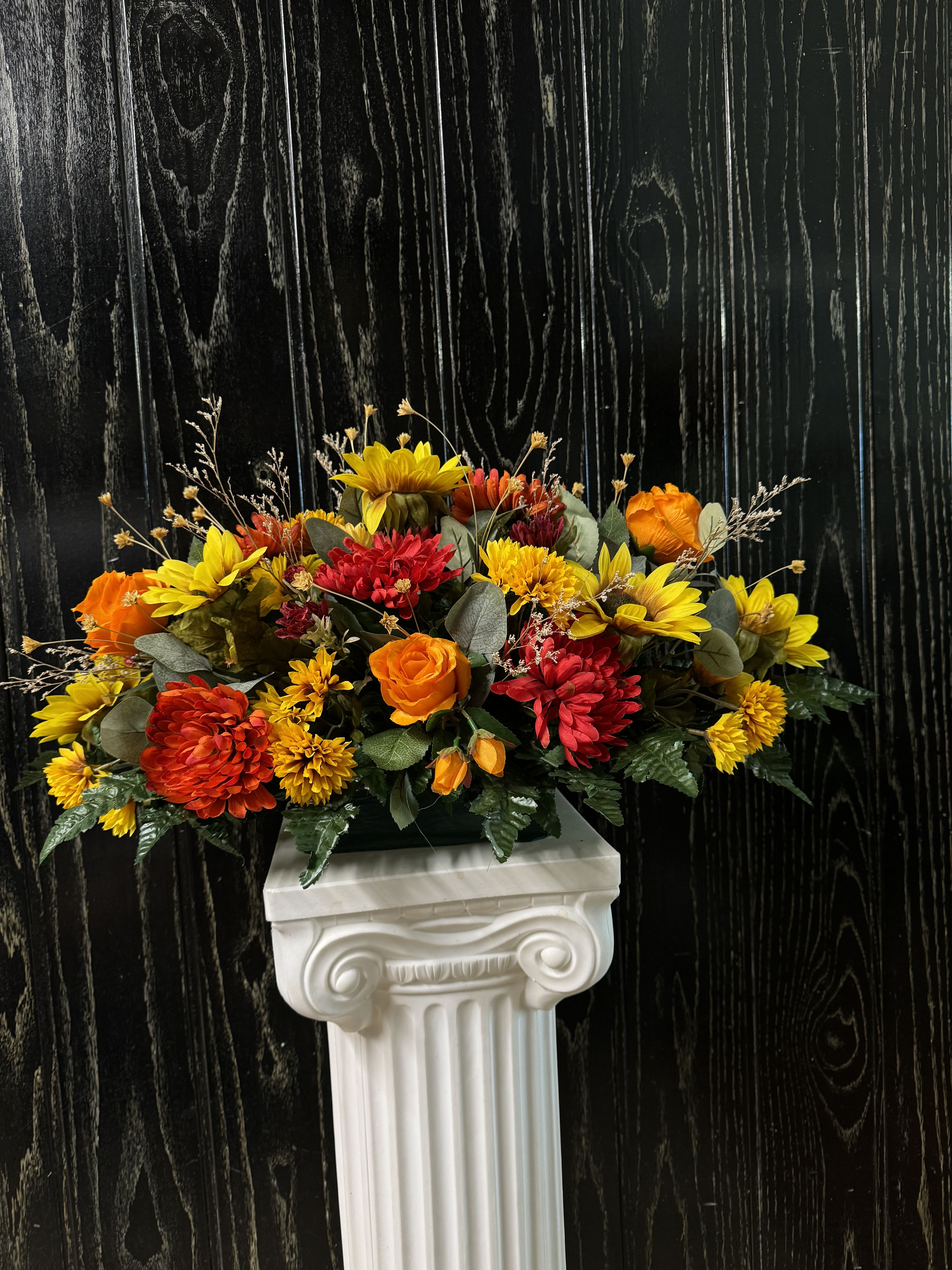 Bright orange and yellow floral arrangement on a white pedestal