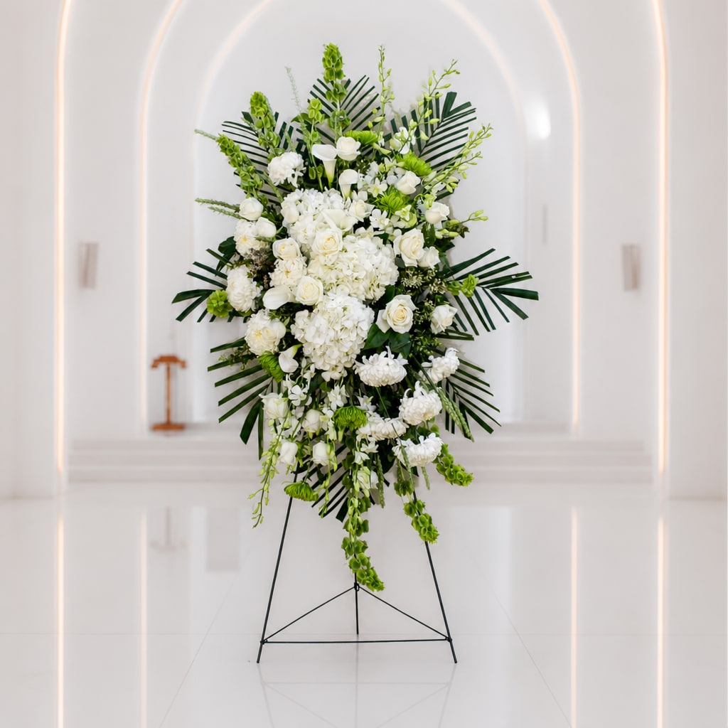 White floral standing spray with green accents on a black easel