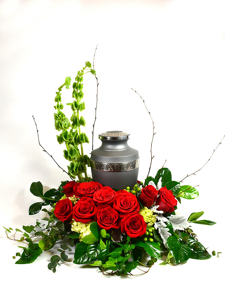 Red roses arranged around a gray urn with tall green accents