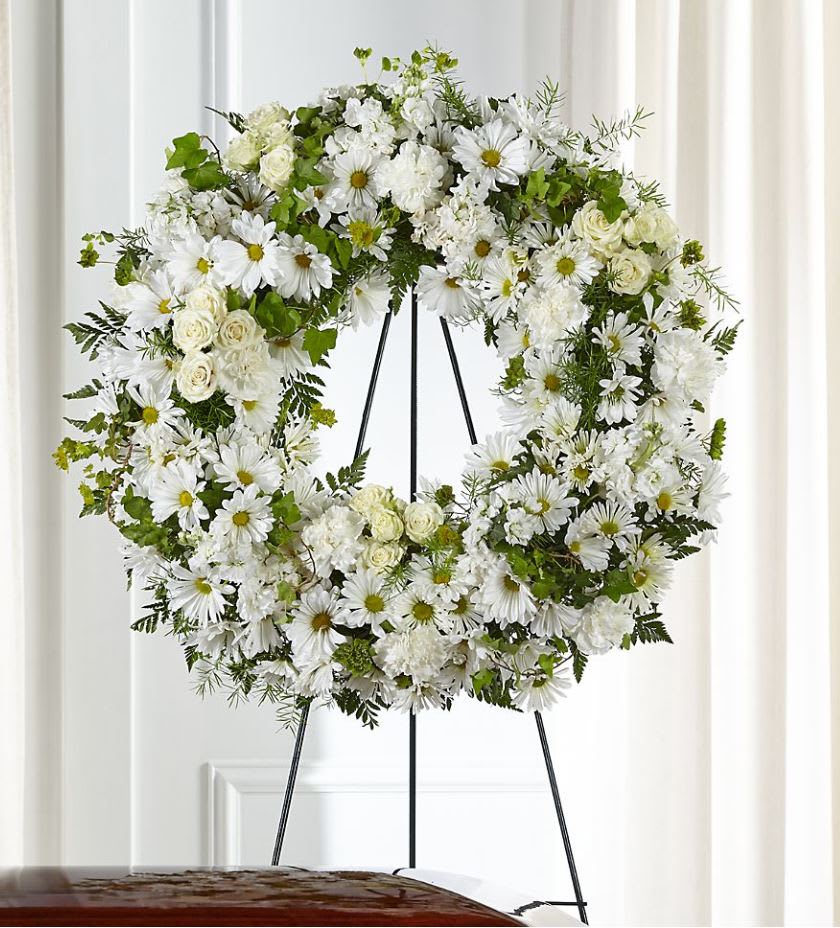 White floral wreath on a black stand with daisies and roses