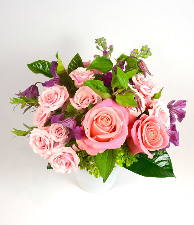 Pink roses and purple flowers arranged in a white vase