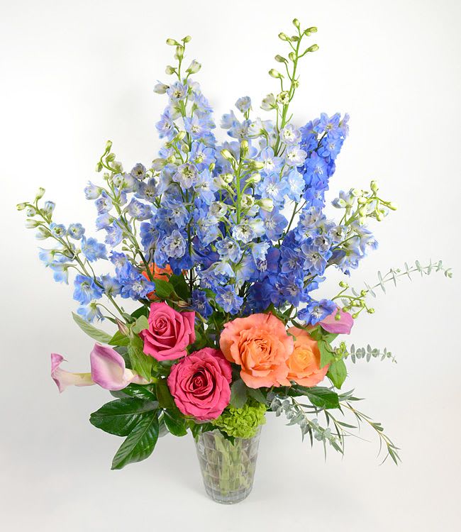 Tall bouquet of blue flowers with pink and peach roses in a clear vase