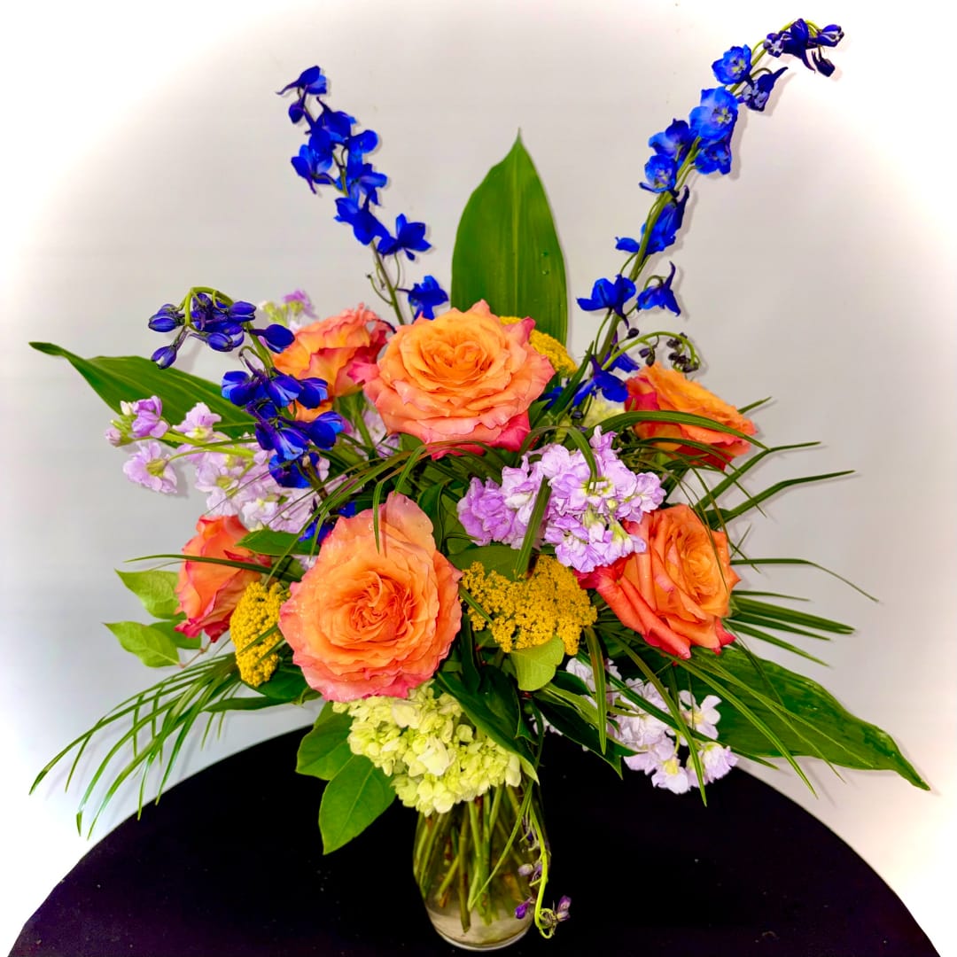 Orange roses and blue flowers in a glass vase