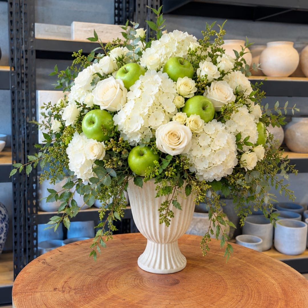 White roses and hydrangeas with green apples in a cream vase