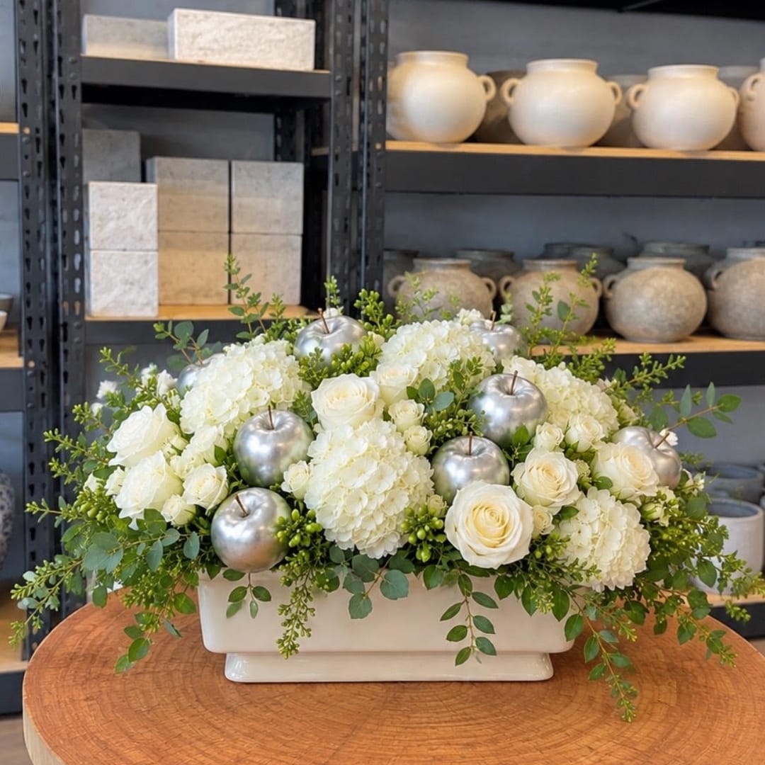 White roses and hydrangeas in a rectangular vase with silver apple accents