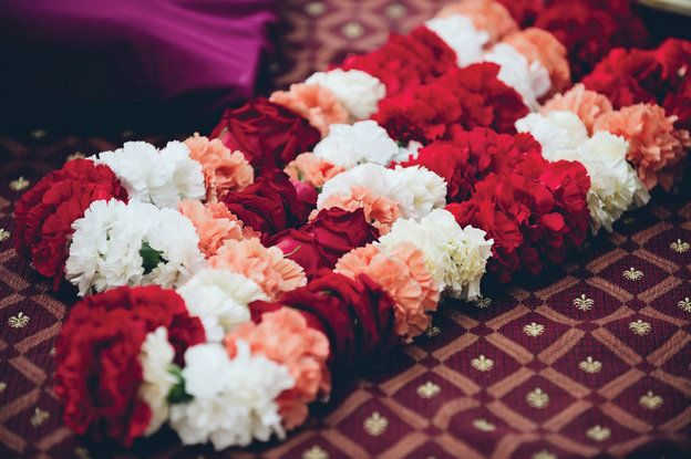 Rows of red, white, and peach flower garlands laid on patterned fabric