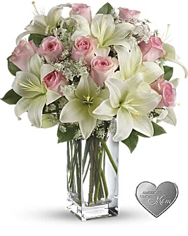 Pink roses and white lilies in a clear glass vase with a heart keepsake