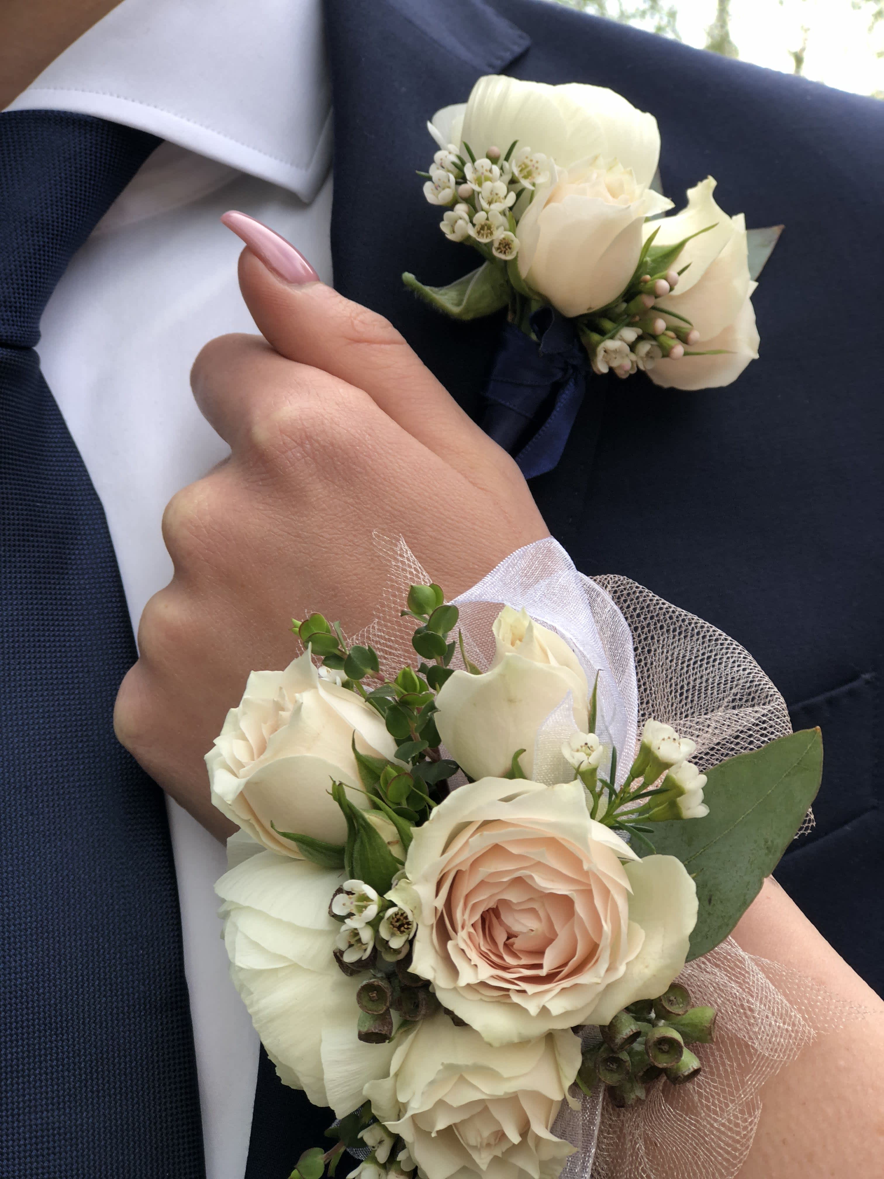 White rose boutonnieres and corsages on a navy suit and wrist