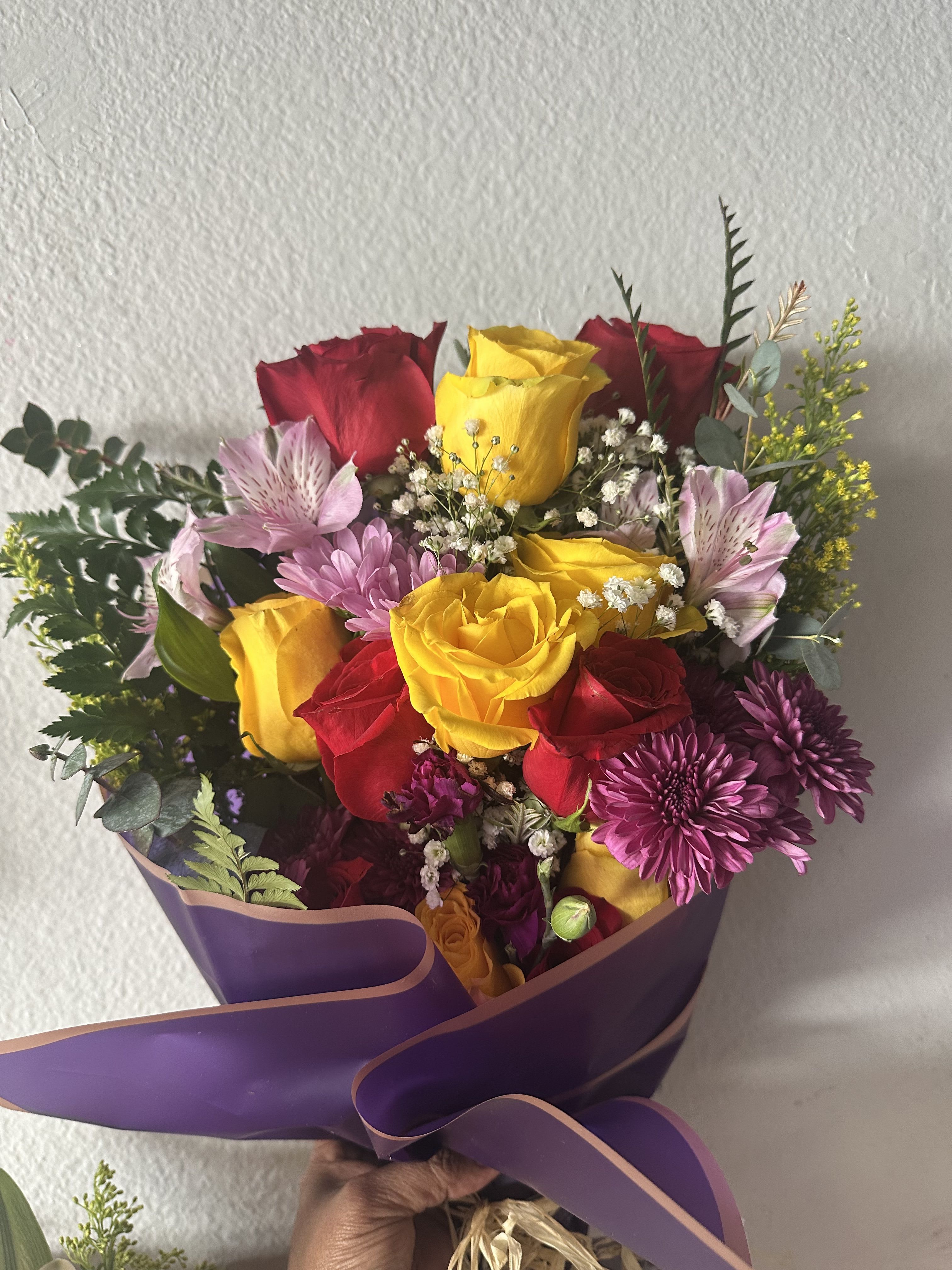 Bouquet of red and yellow roses with purple flowers wrapped in purple paper