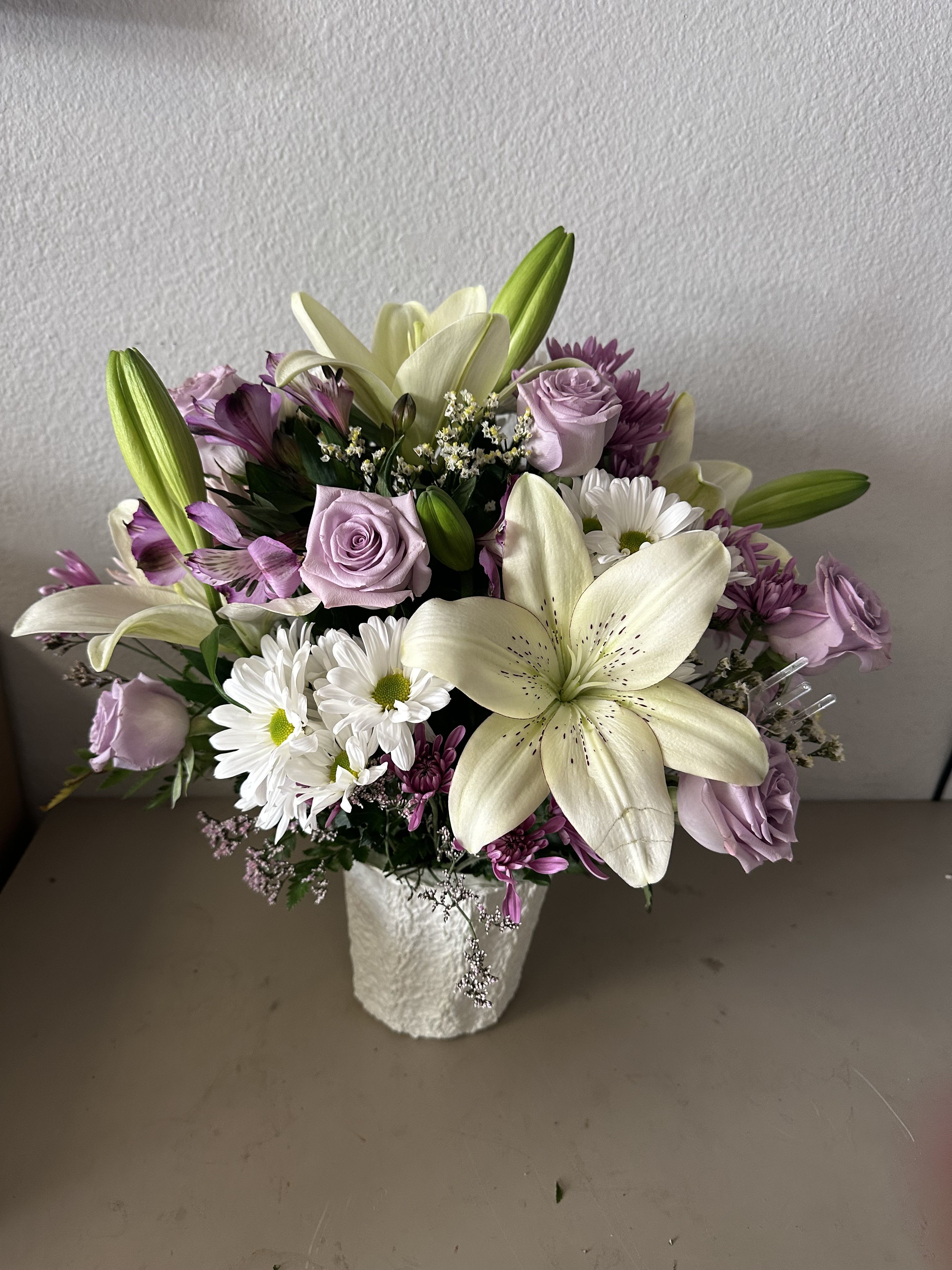 Bouquet of white lilies, lavender roses, and white daisies in a white vase
