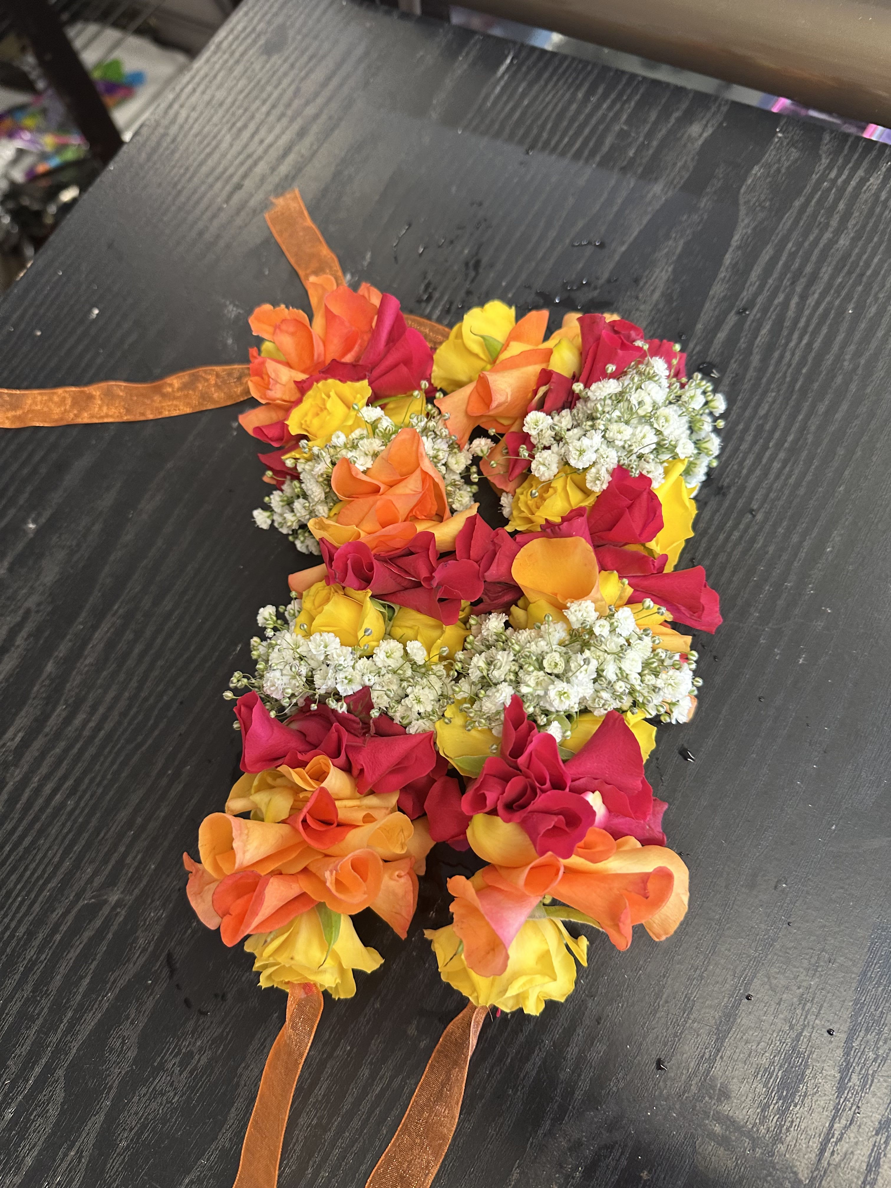 Colorful floral lei made of roses and baby's breath with orange ribbon ties