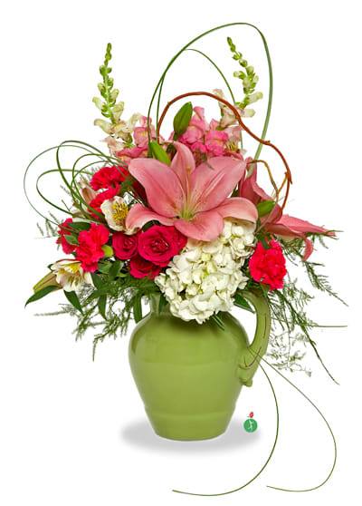 Tall arrangement of pink lilies, red roses and white hydrangeas in a green ceramic pitcher