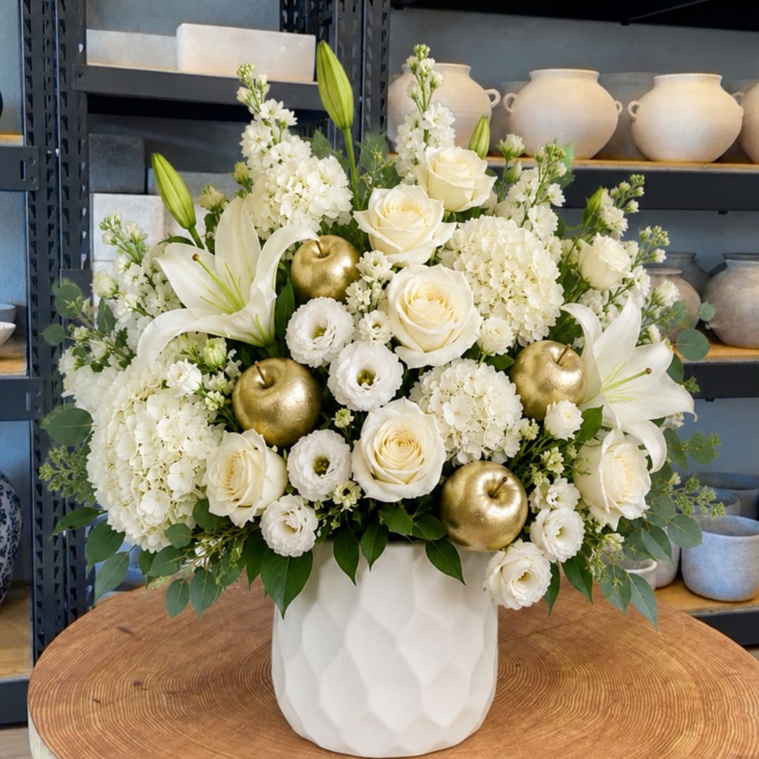 White floral arrangement with roses, lilies, and gold apple accents in a white vase