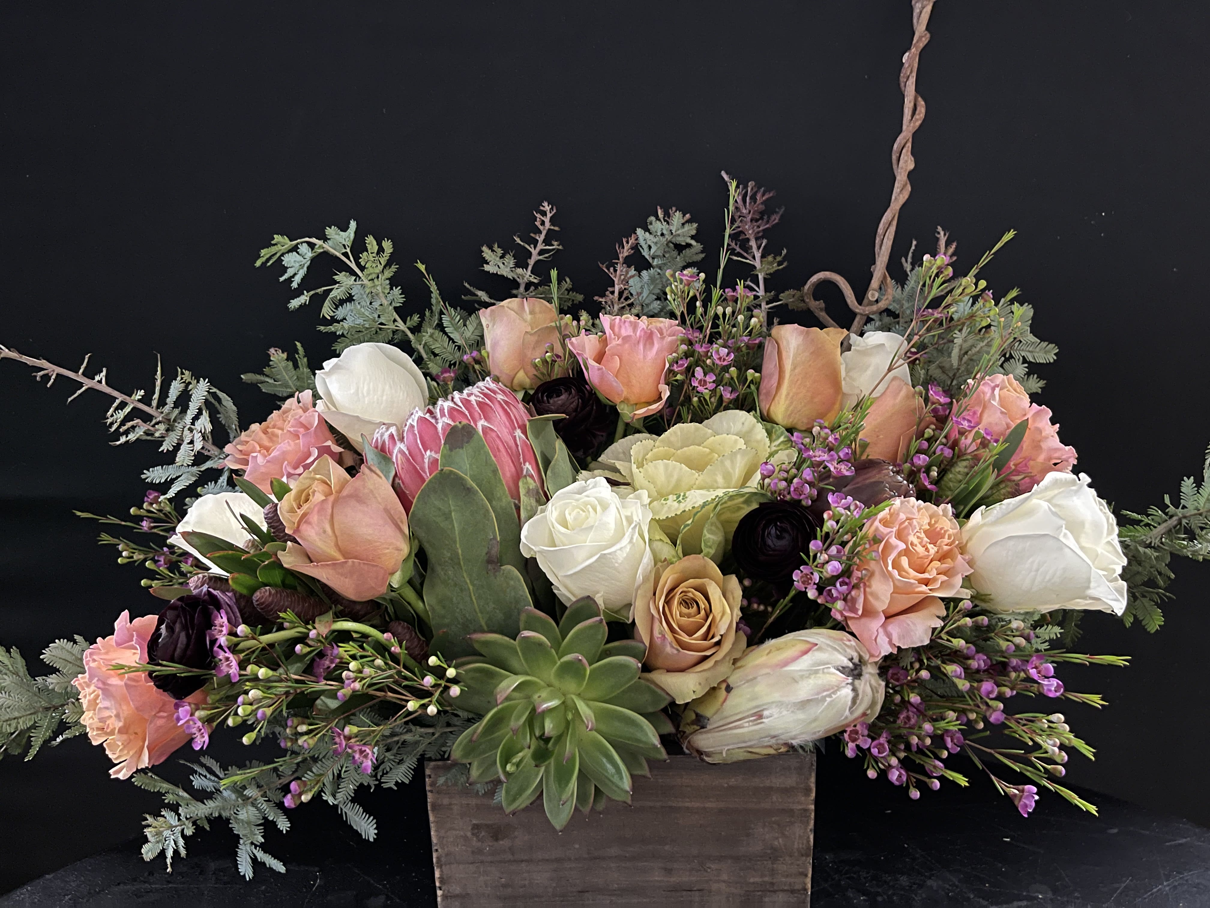 Low arrangement of peach and white roses with protea and succulents in a rustic wooden box