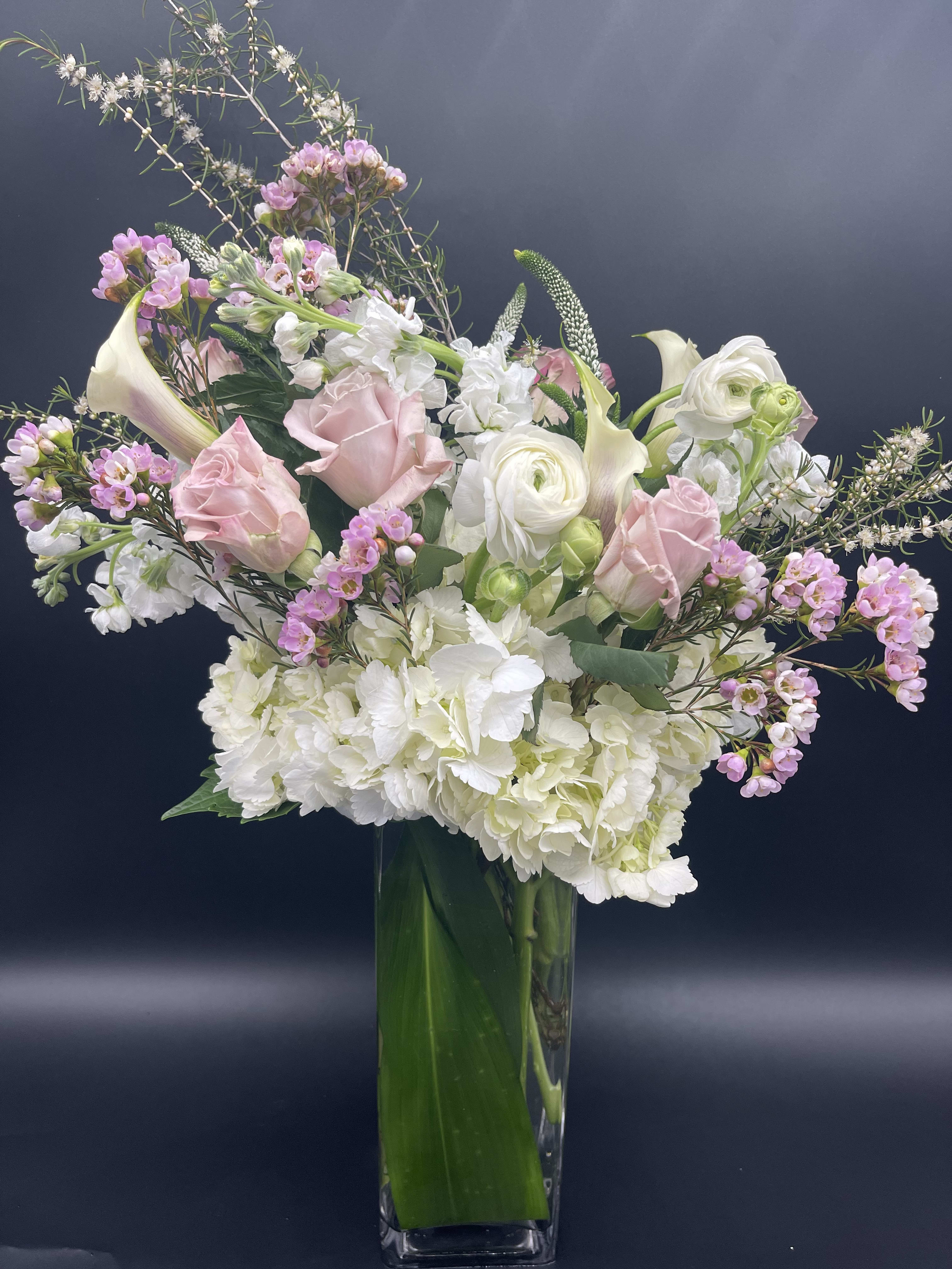 Tall vase arrangement with white hydrangeas, pink roses, calla lilies, and mixed white and pink blooms