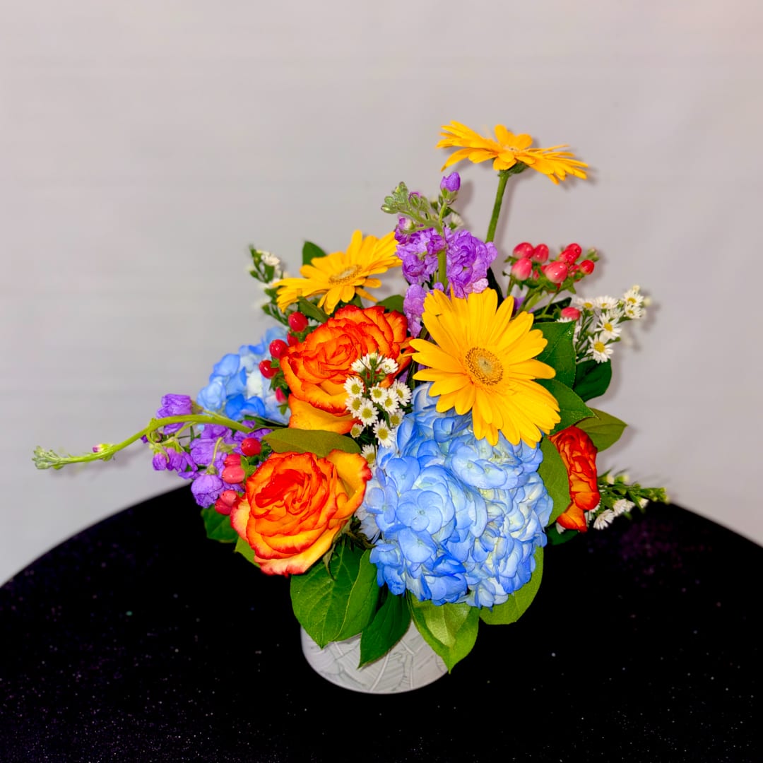 Colorful bouquet with yellow daisies, orange roses, and blue hydrangea in a white vase