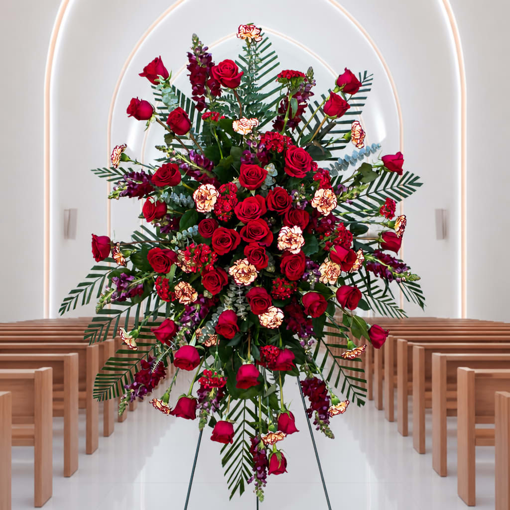 Large standing floral spray with red roses and purple accents in a church aisle