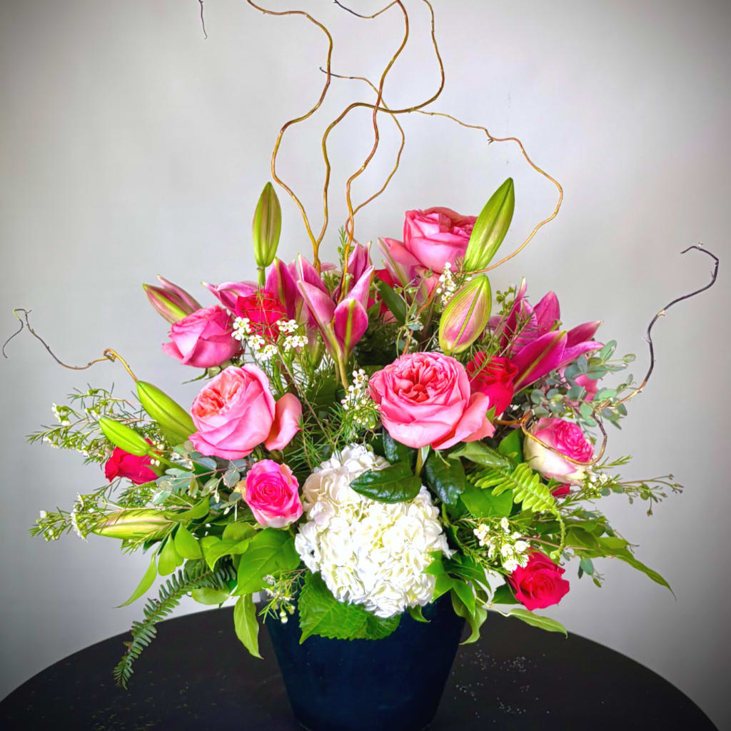 Pink roses and lilies arranged in a dark vase with white hydrangea