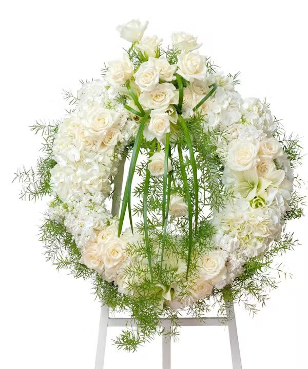 White rose and hydrangea wreath with green ribbon on a stand