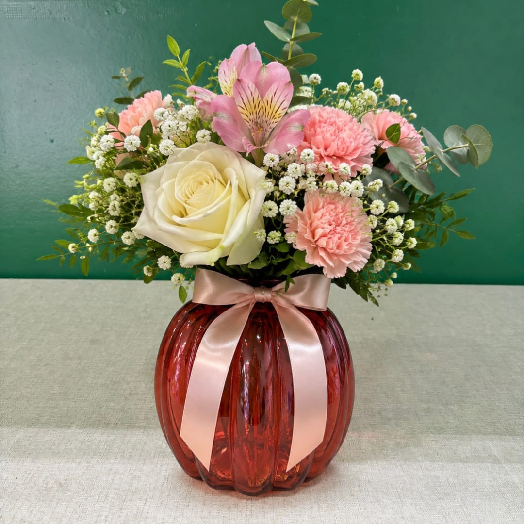 Pink and white flower arrangement in a red glass vase with a ribbon