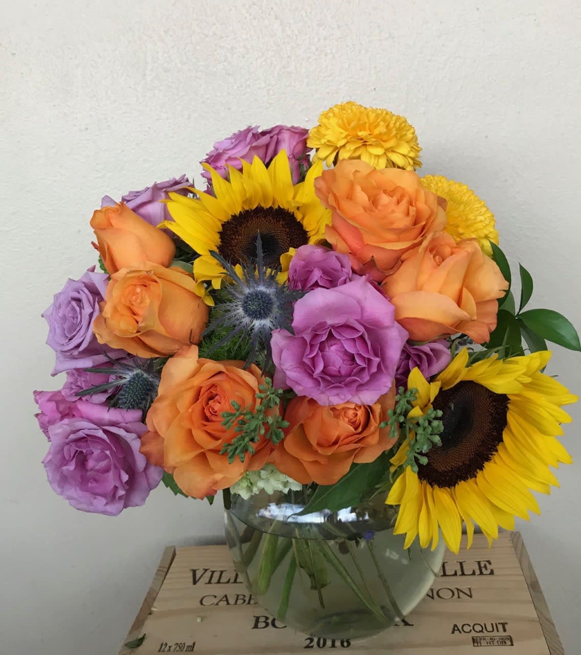 Bouquet of orange and purple roses with sunflowers in a glass vase