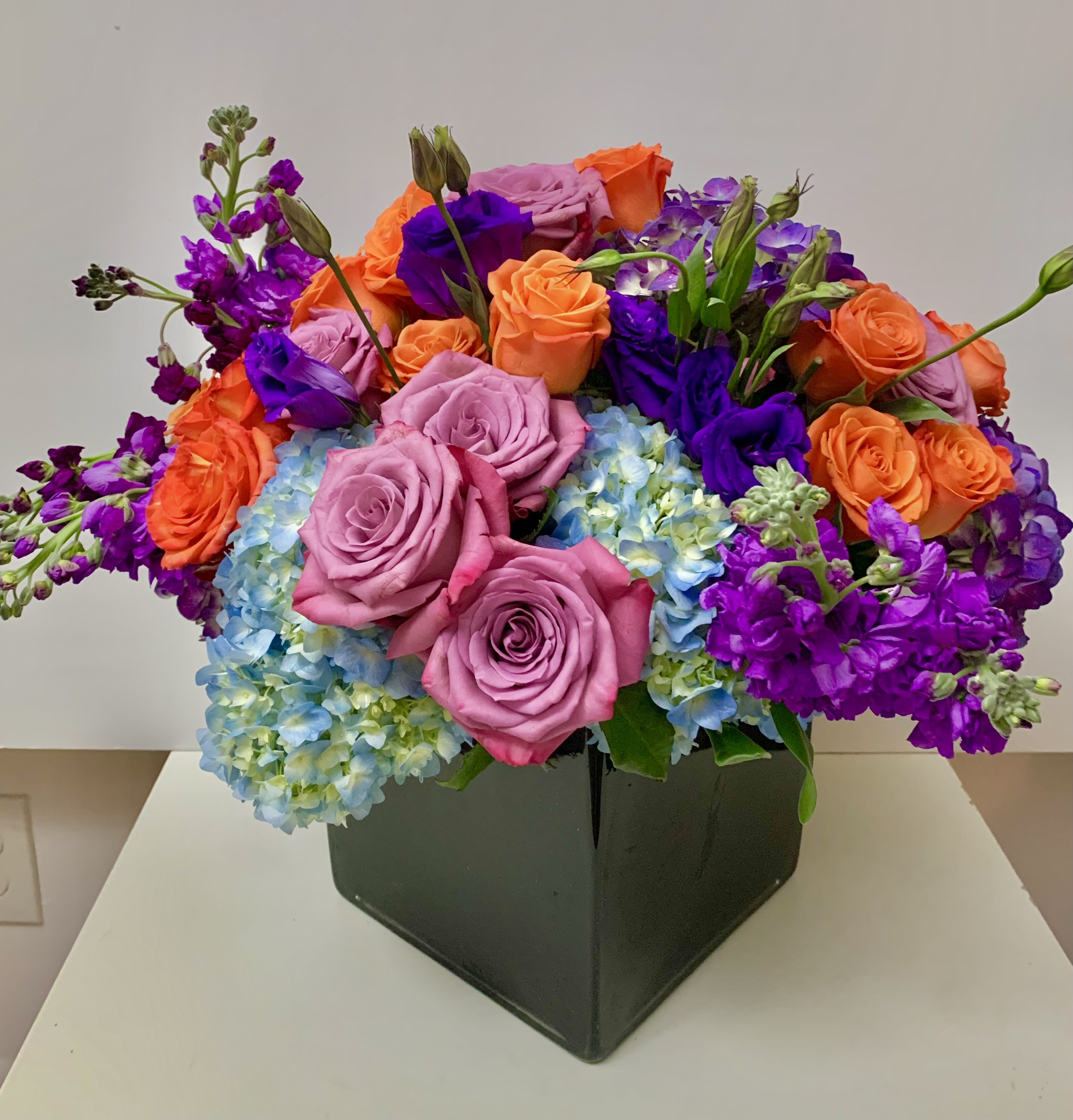 Colorful bouquet of roses, hydrangeas, and purple blooms in a black box