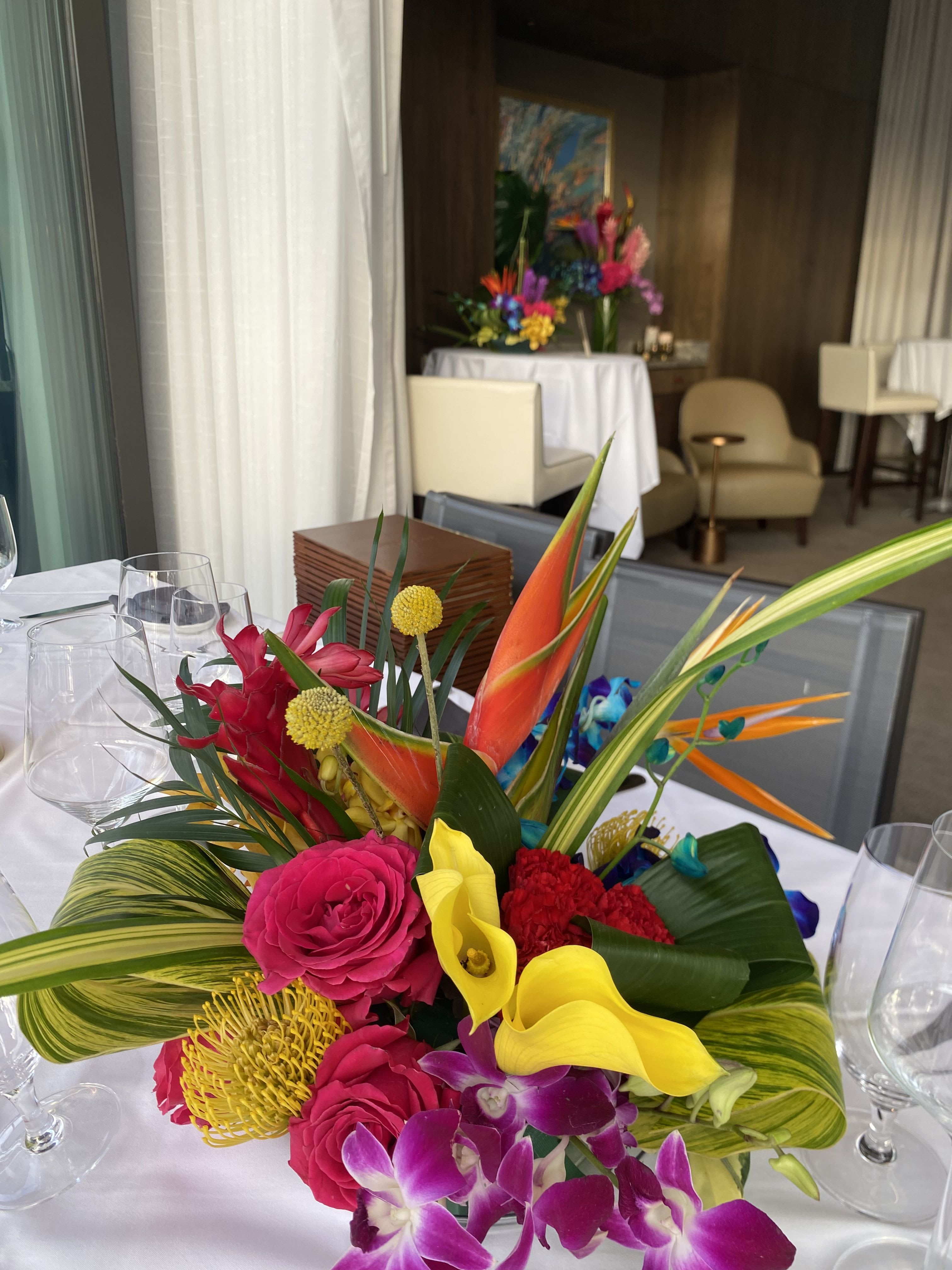Bright tropical centerpiece with orchids, calla lilies, and roses on a dining table