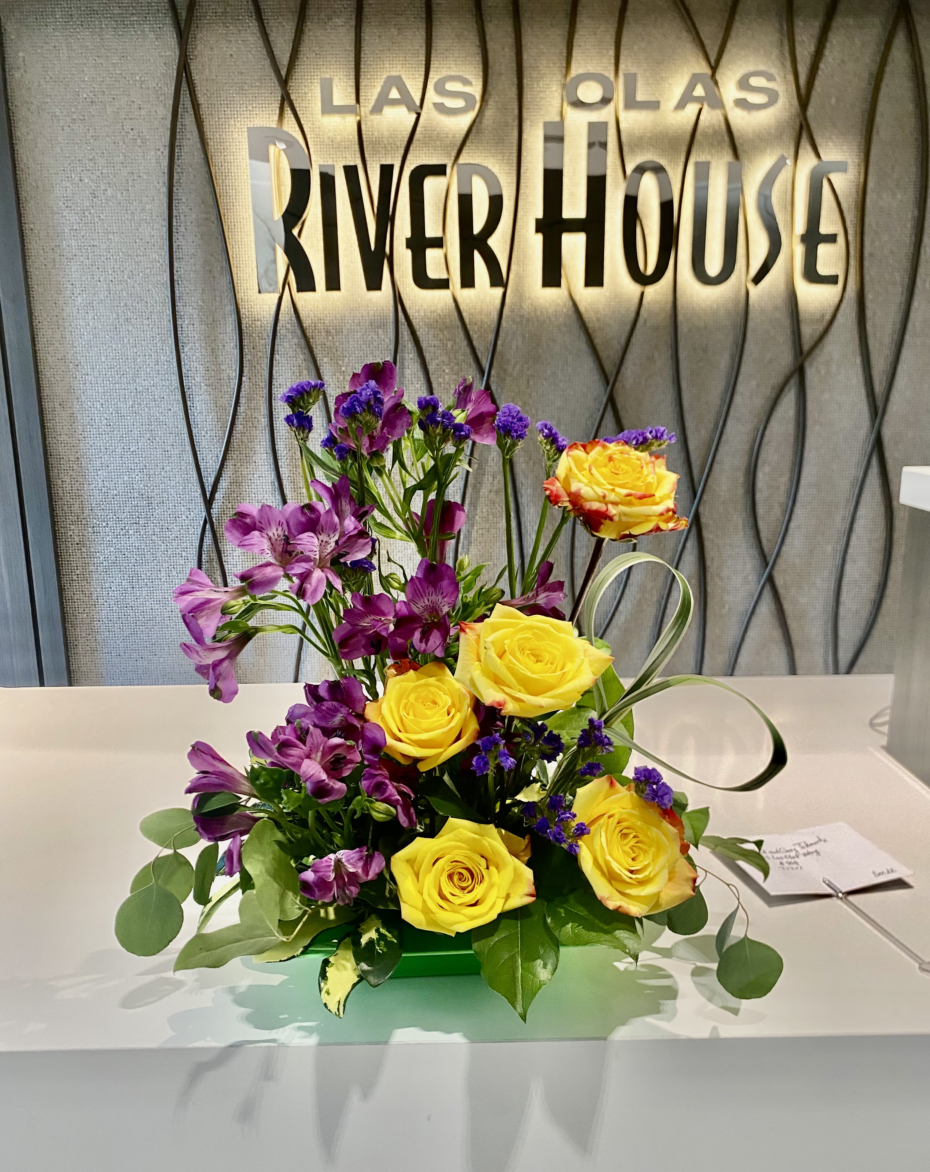 Yellow roses and purple flowers arranged in a low centerpiece