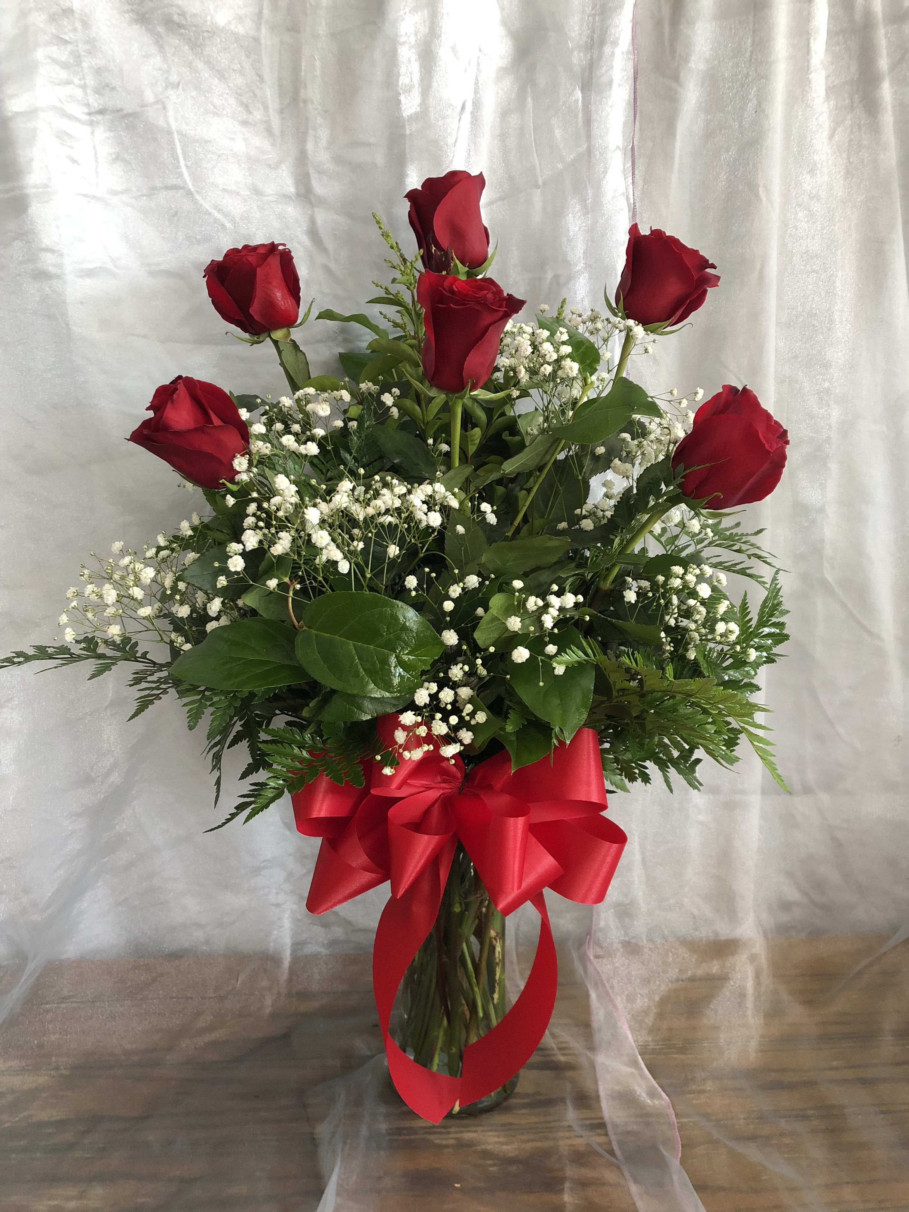 Red roses in a glass vase with baby's breath and a red ribbon