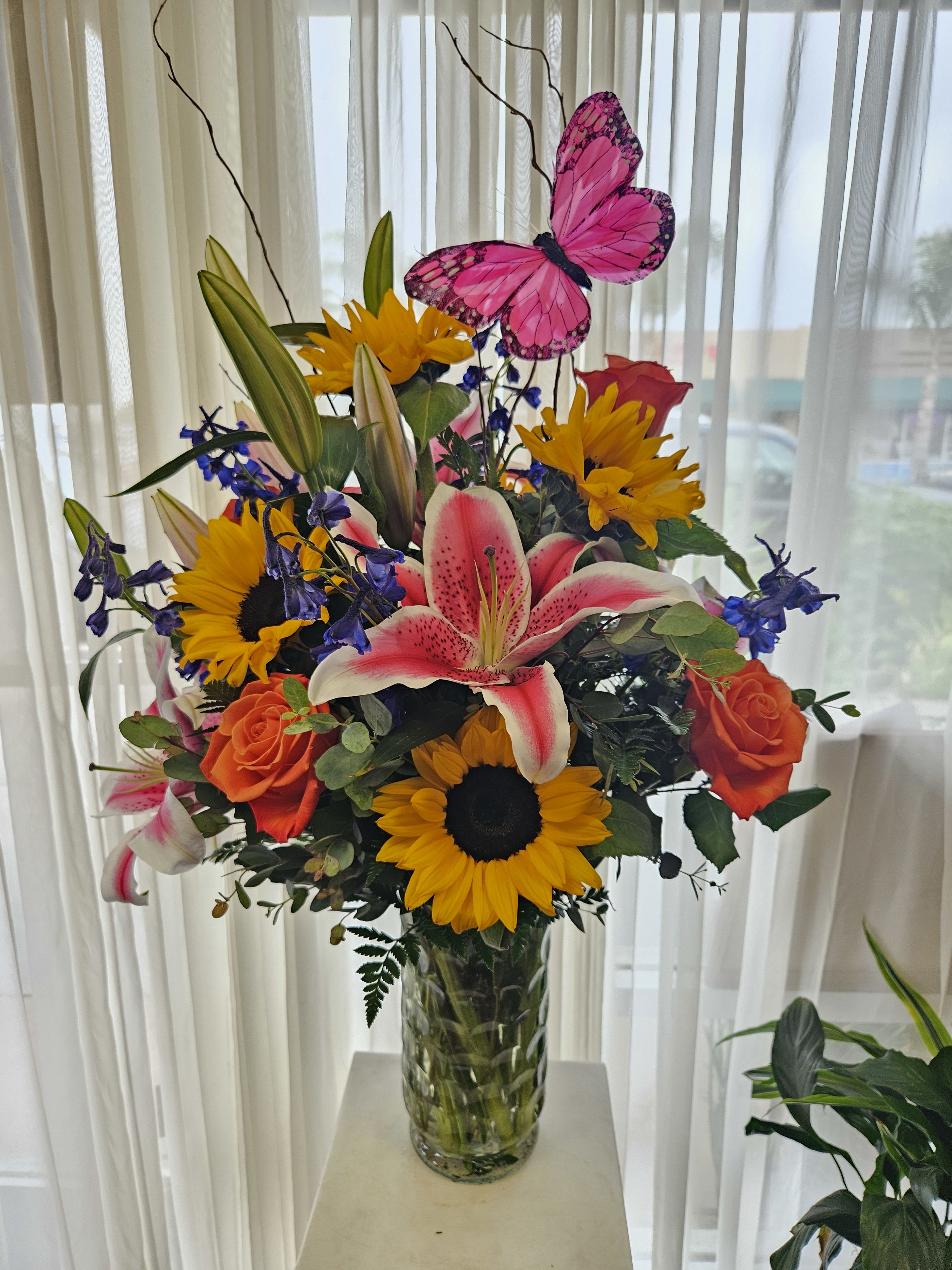Bright mixed bouquet in a glass vase with a pink butterfly pick