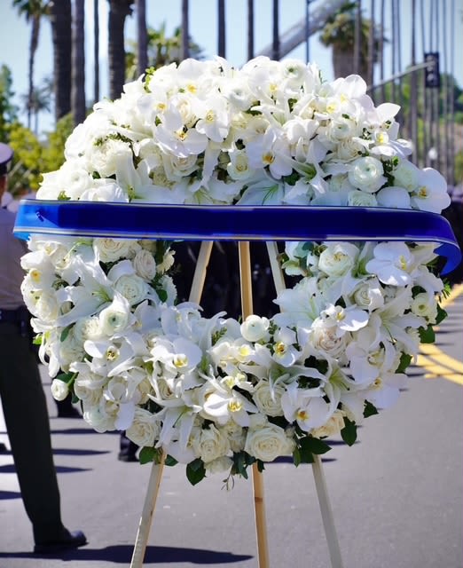 White floral funeral wreath on an easel with a blue ribbon