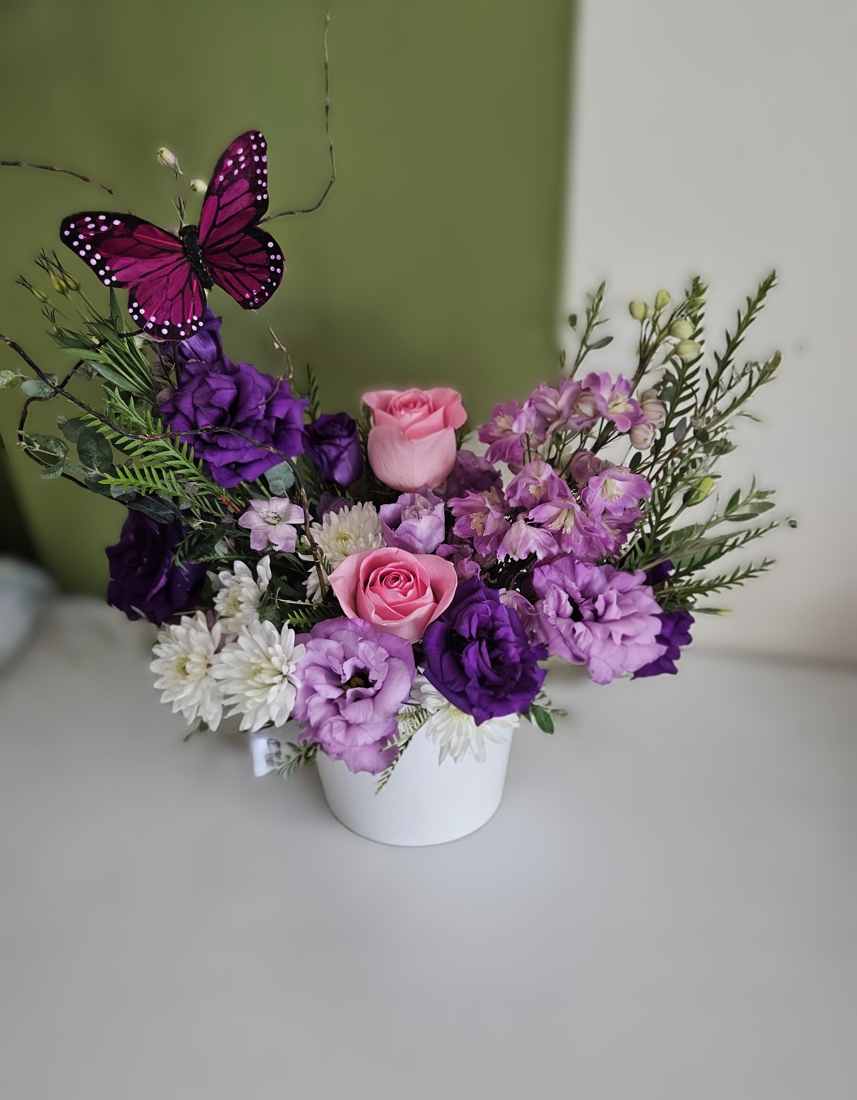 Purple and pink flower arrangement in a white pot with a butterfly pick
