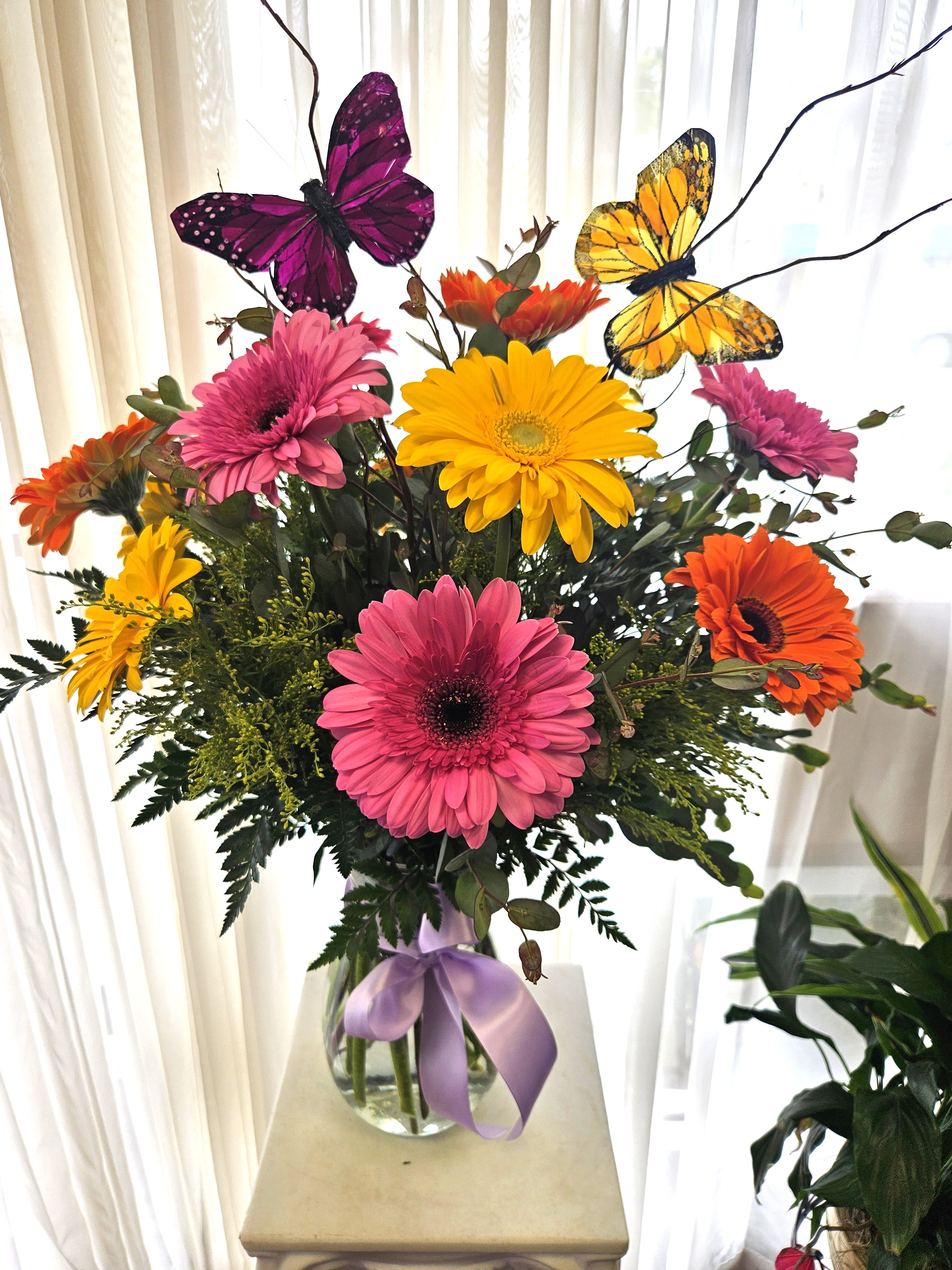 Bouquet of colorful gerbera daisies in a glass vase with butterfly picks