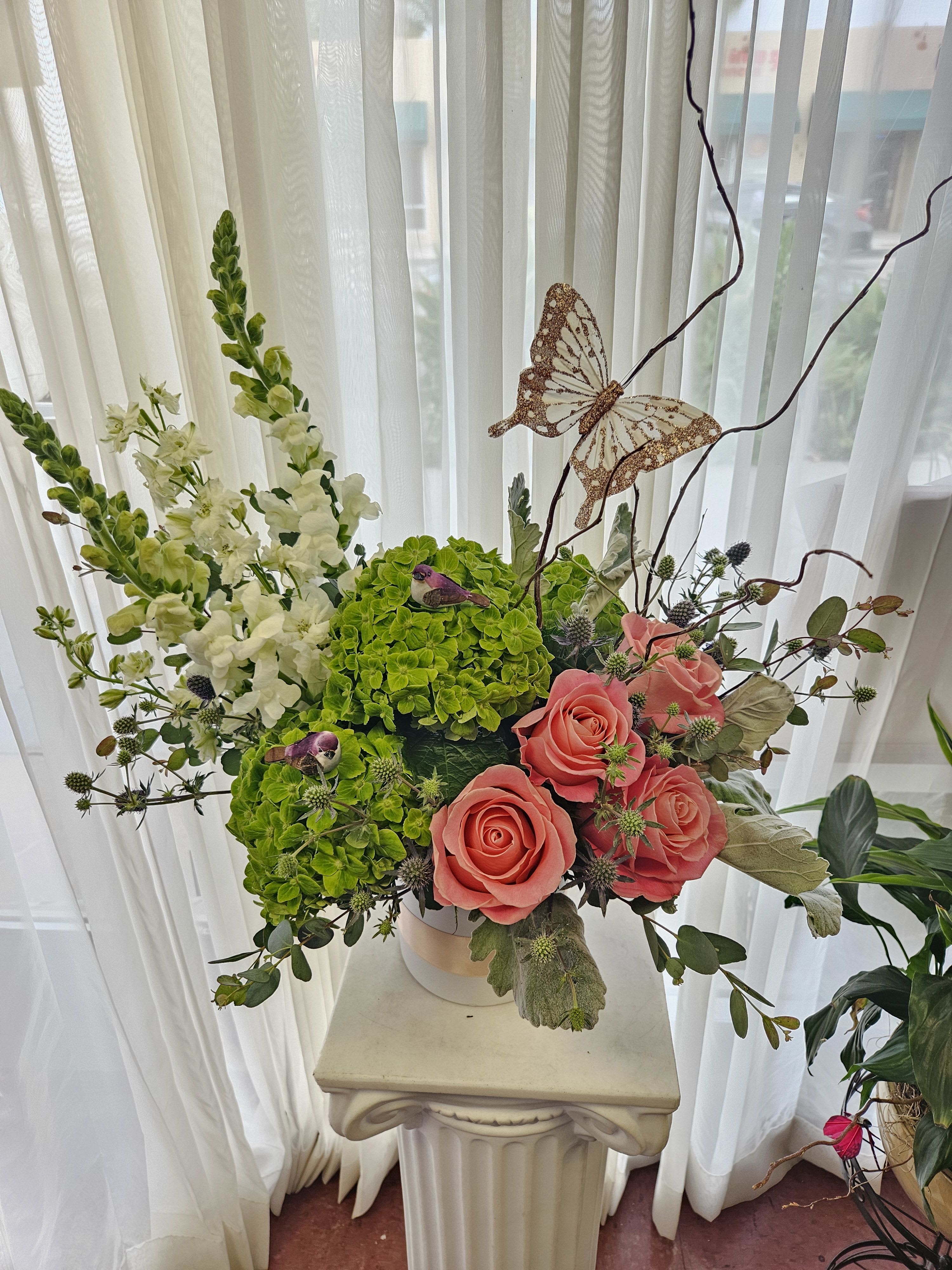Pink roses and green hydrangeas in a white vase with a butterfly accent