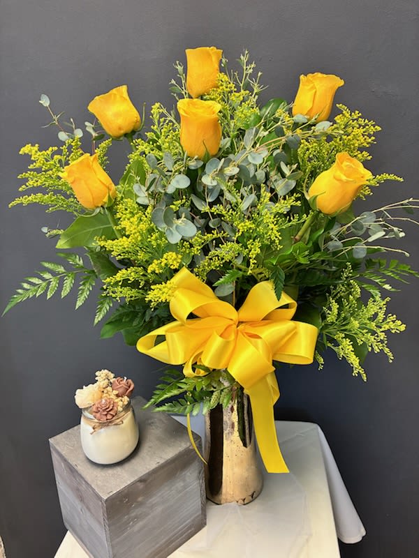 Yellow roses arranged in a tall vase with a large yellow ribbon