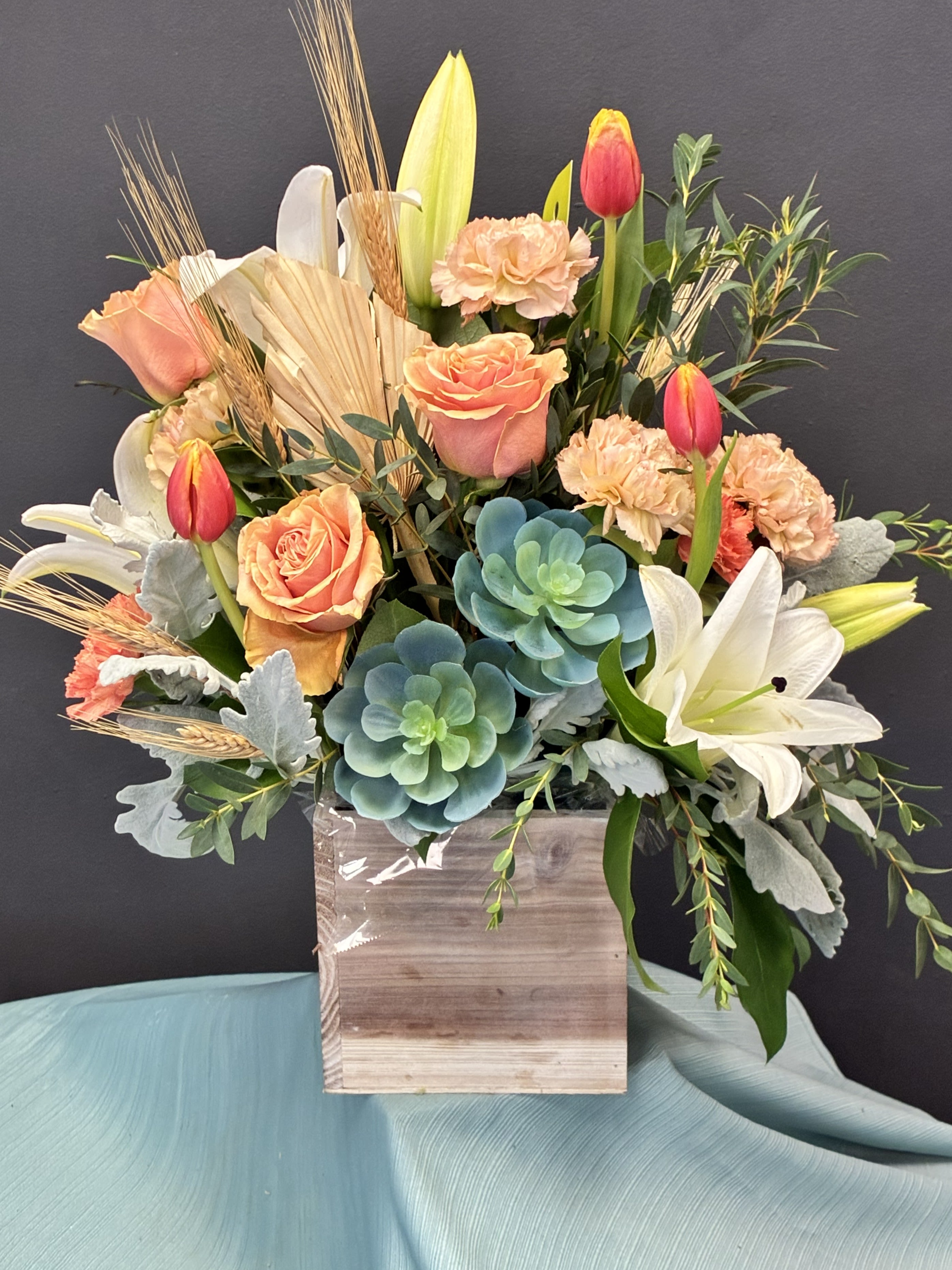 Mixed bouquet with roses, tulips, lilies, and succulents in a wooden box