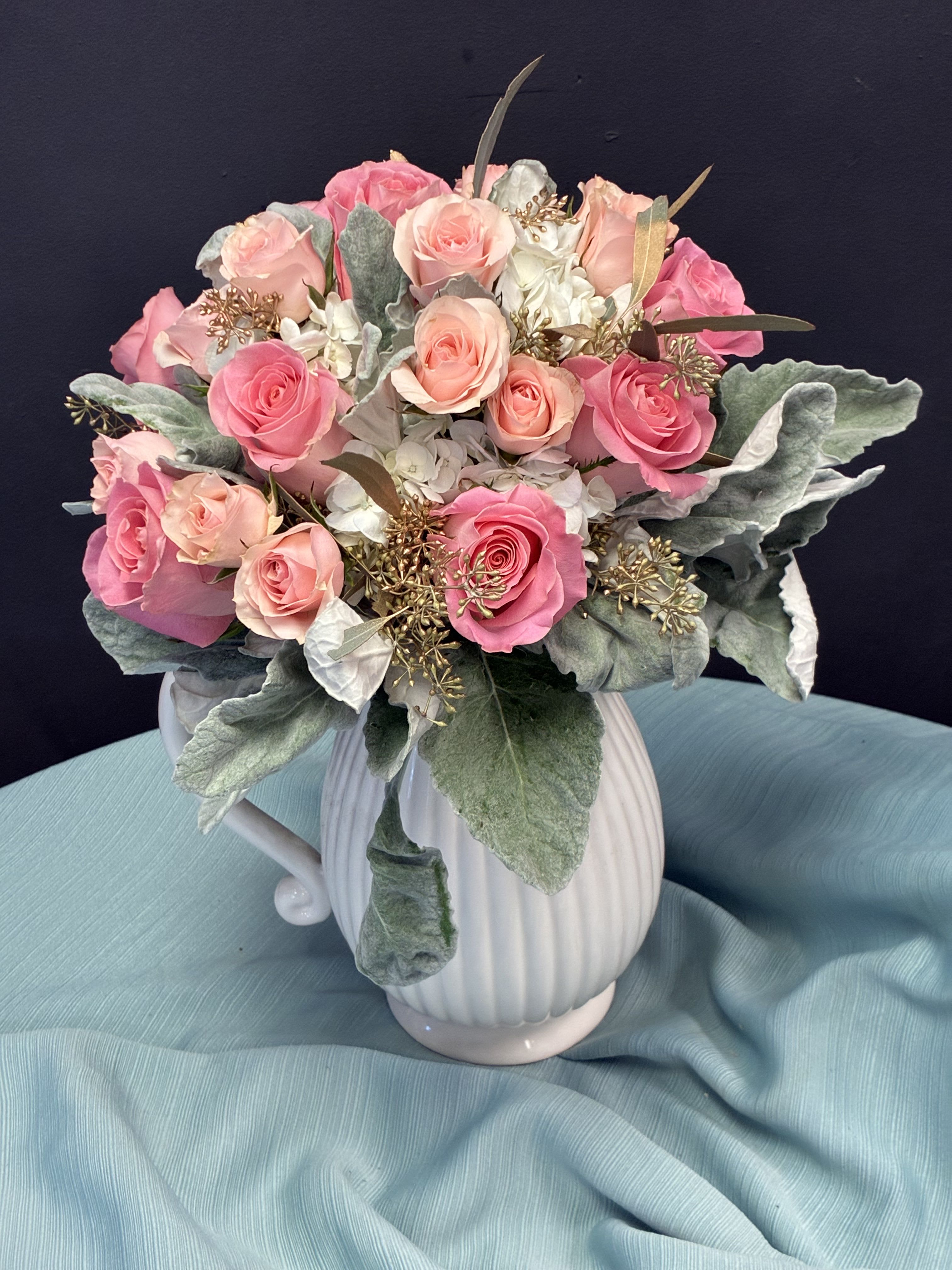 Pink and peach roses arranged in a white ceramic pitcher