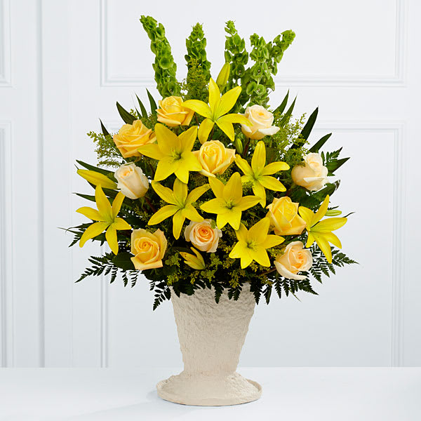 Yellow lilies and pale roses arranged in a cream vase