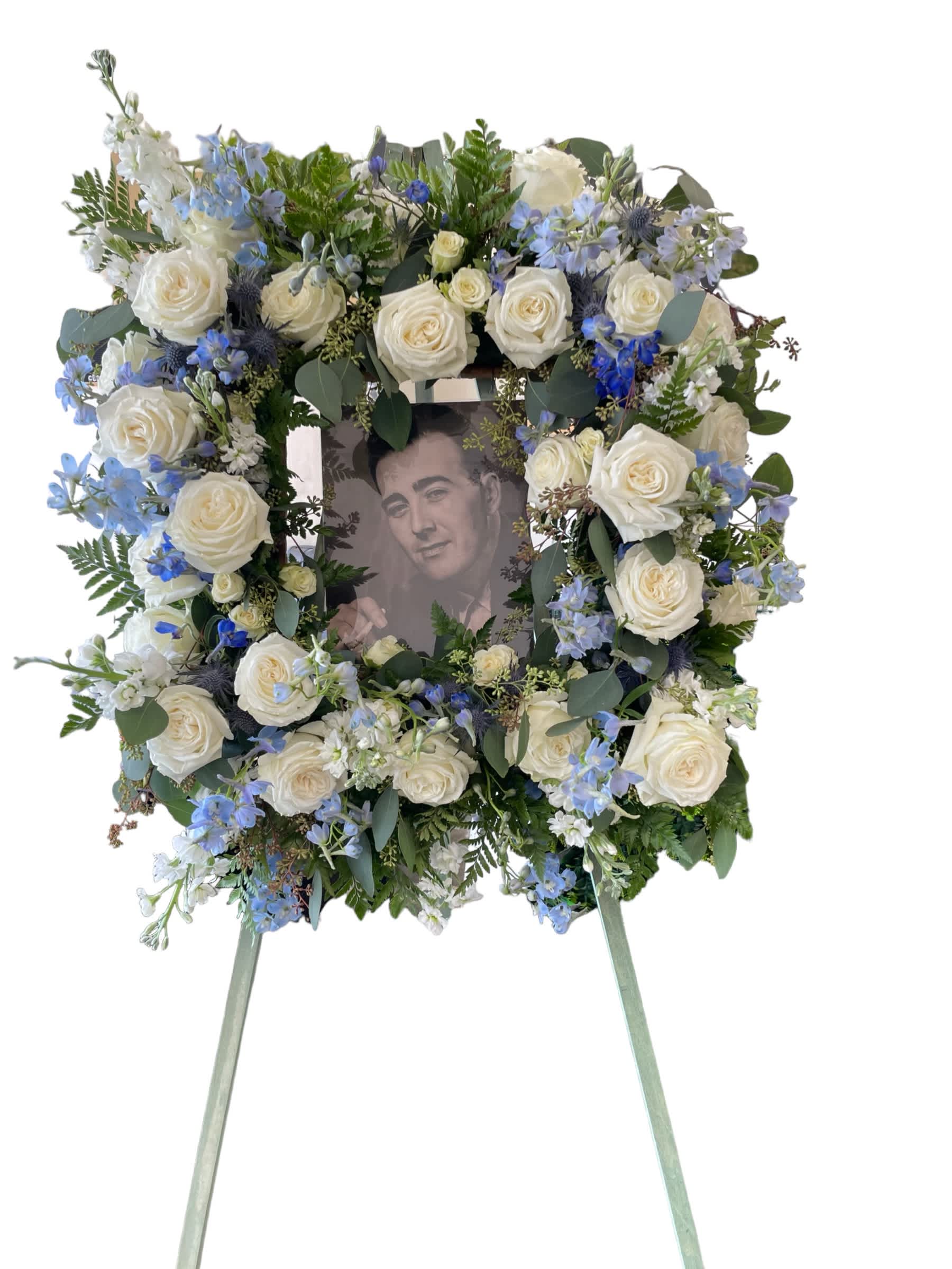 Large floral wreath with white roses and blue flowers around a portrait