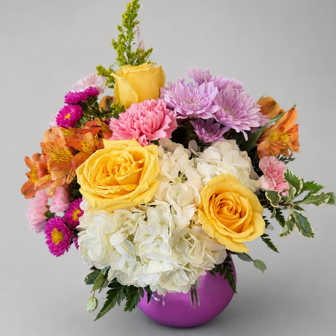 Colorful bouquet of yellow roses, hydrangeas, and mixed blooms in a purple vase